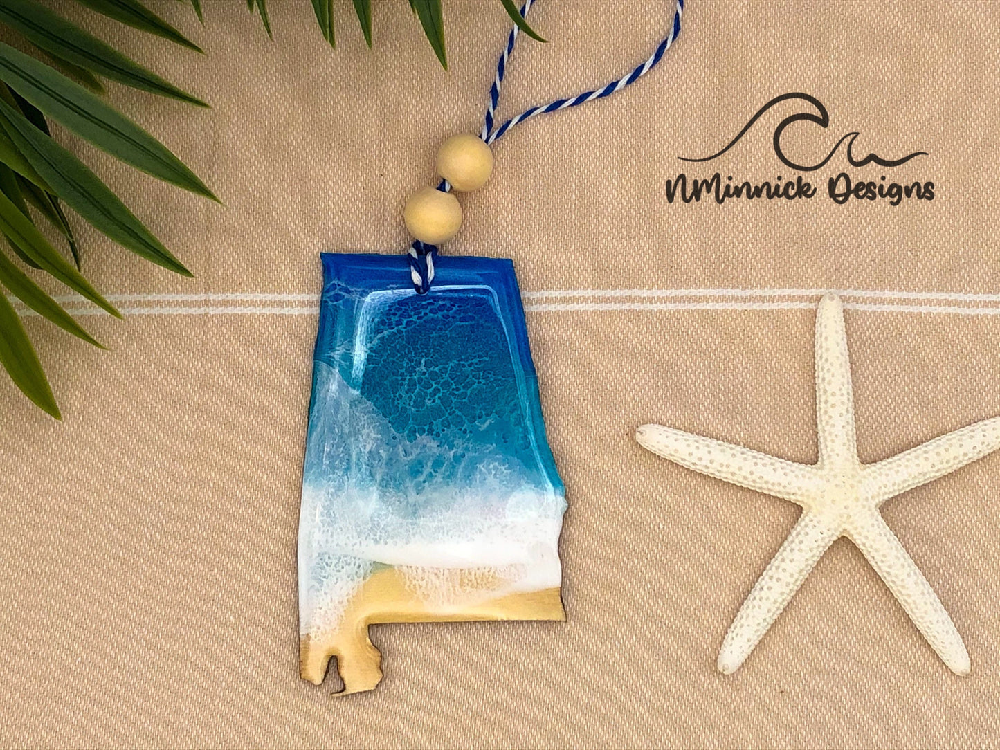 Alabama shaped laser cut wood ornament with a blue and teal beach scene made with epoxy resin. Finished with bakers twine and two wood beads.