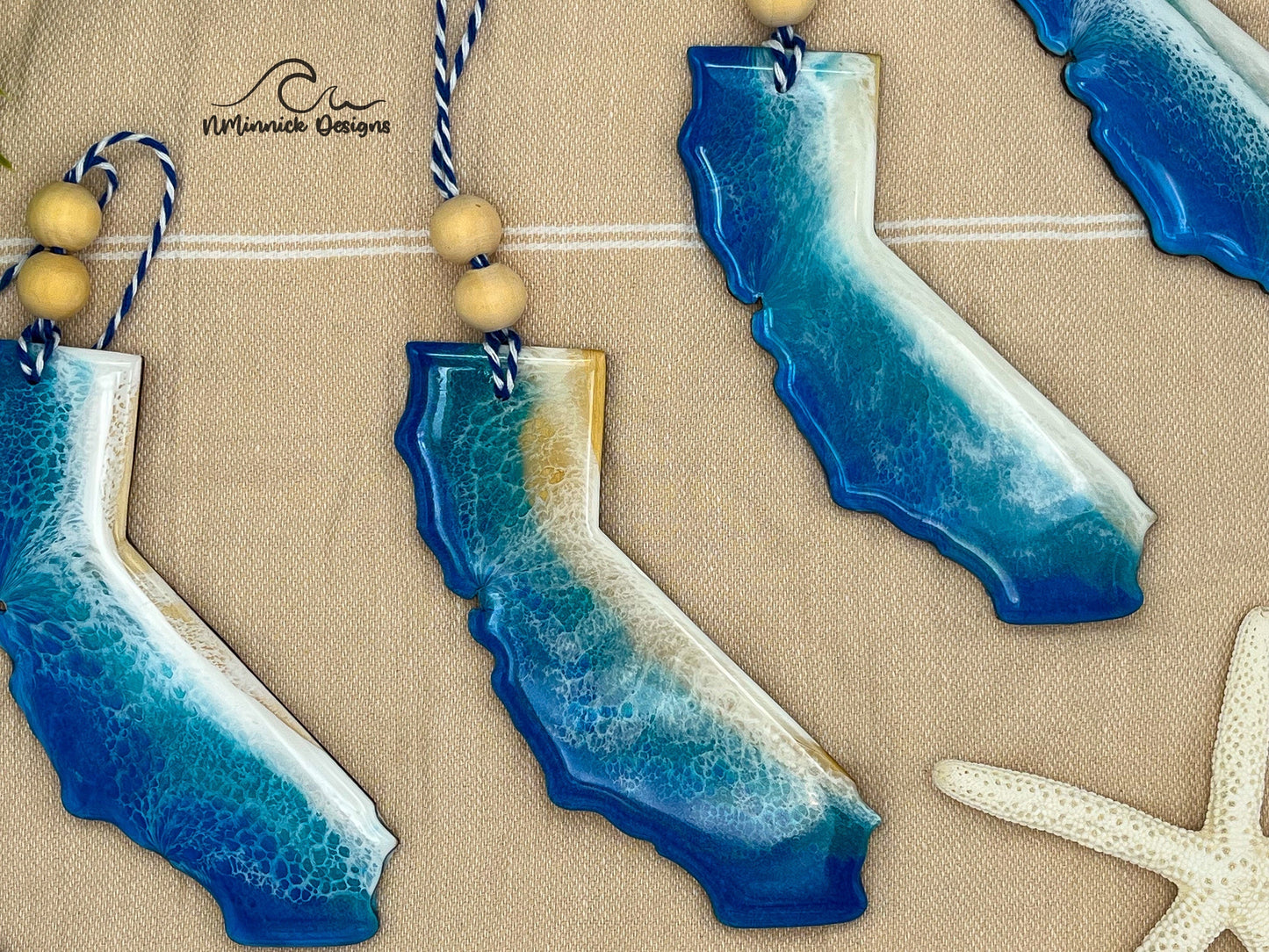 California-shaped wooden Christmas ornament covered in blue and teal colored ocean resin art resembling the waves along California's Pacific Coast. Finished with blue and white baker's twine and two wooden beads.