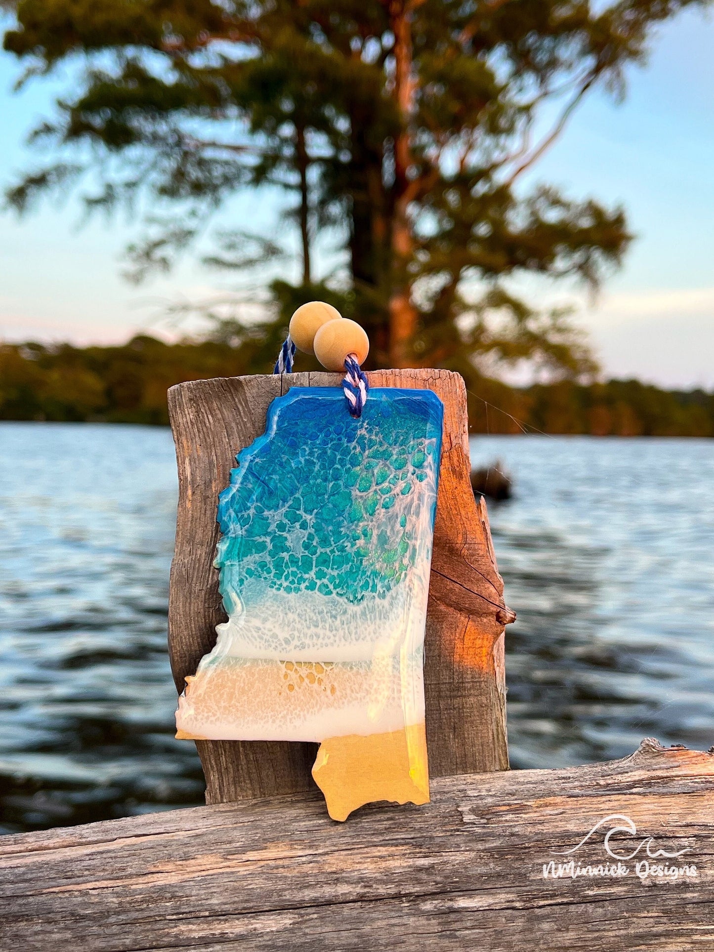 Mississippi-shaped wooden Christmas ornament covered in blue and teal colored ocean resin art resembling the waves along Mississippi's Gulf Coast. Finished with blue and white baker's twine and two wooden beads.