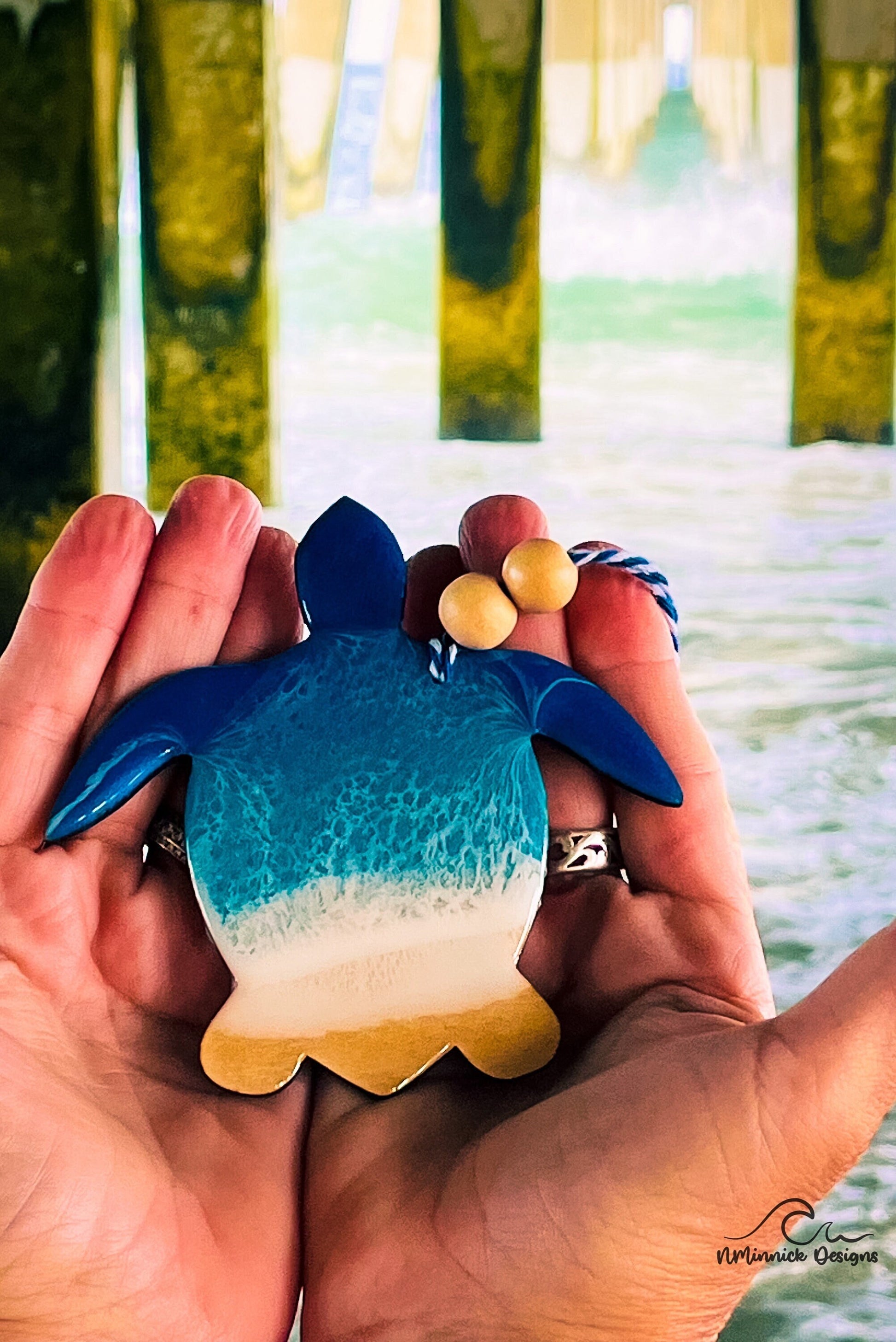 Sea Turtle-shaped wooden Christmas ornament covered in blue and teal colored ocean resin art resembling the waves of the ocean. Finished with blue and white baker's twine and two wooden beads.