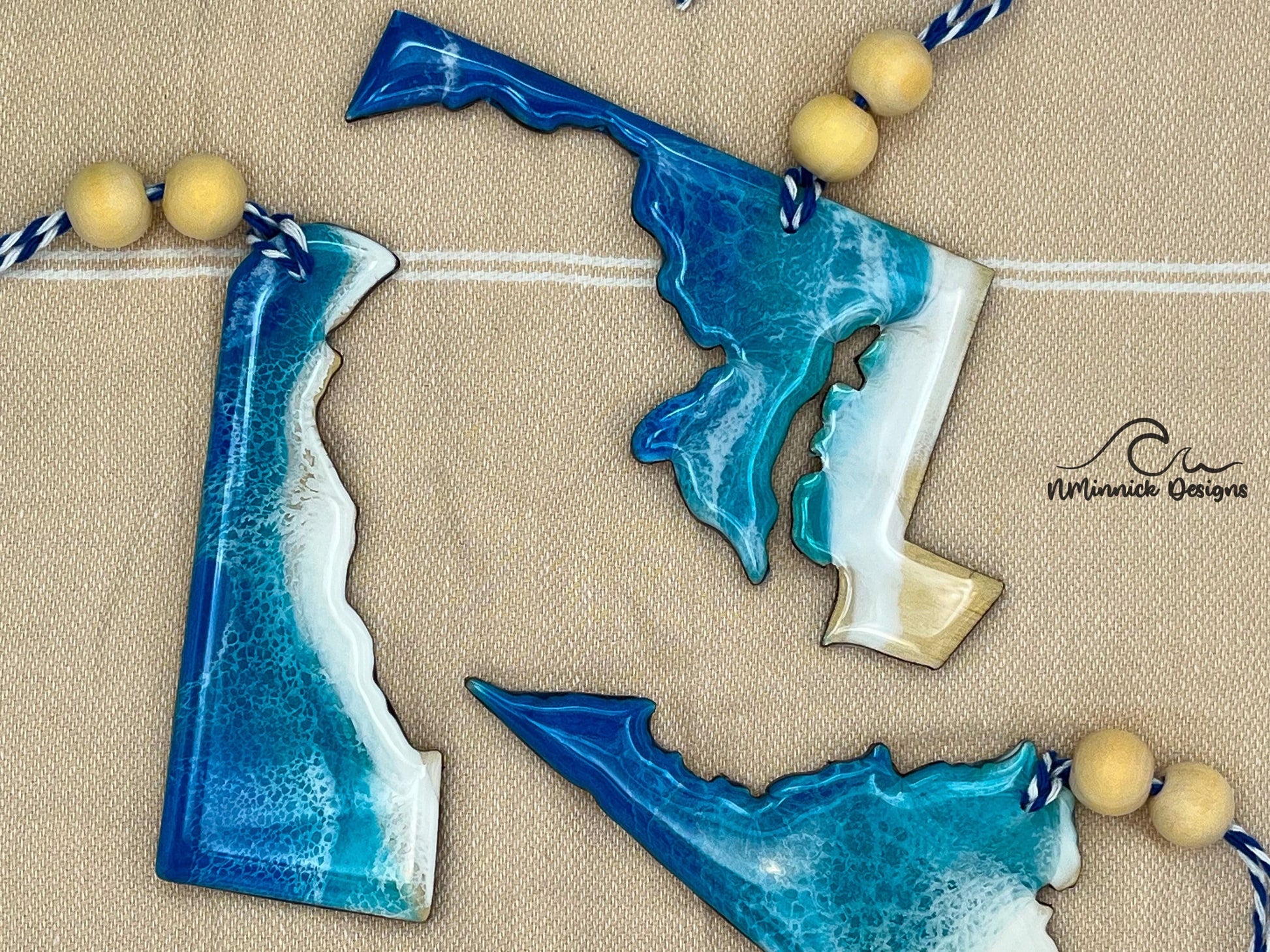 Maryland-shaped wooden Christmas ornament covered in blue and teal colored ocean resin art resembling the waves along Maryland's Atlantic Coast. Finished with blue and white baker's twine and two wooden beads.