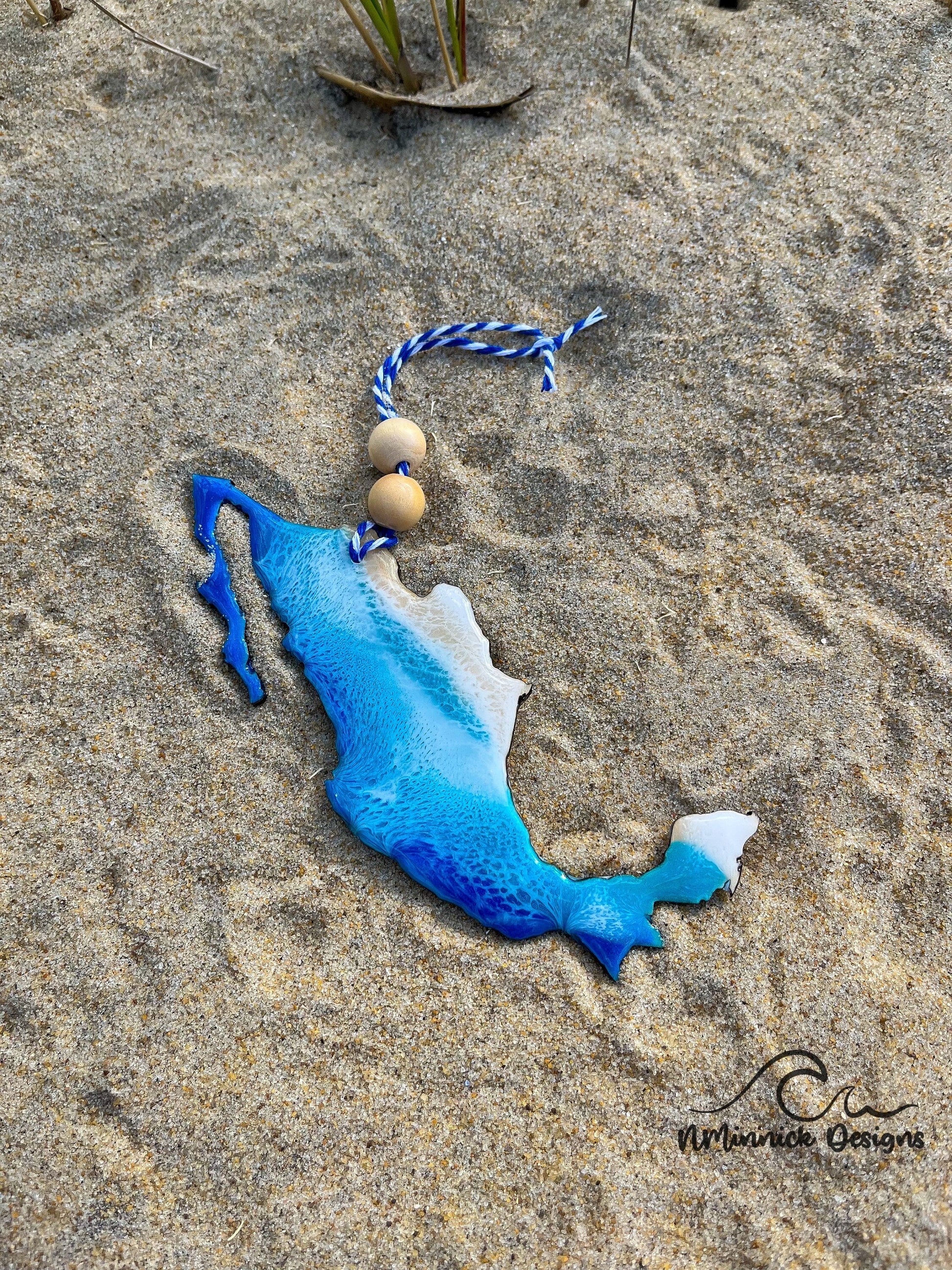 Mexico-shaped wooden Christmas ornament covered in blue and teal ocean resin art resembling the waves of the ocean. Finished with blue and white baker's twine and two wooden beads.