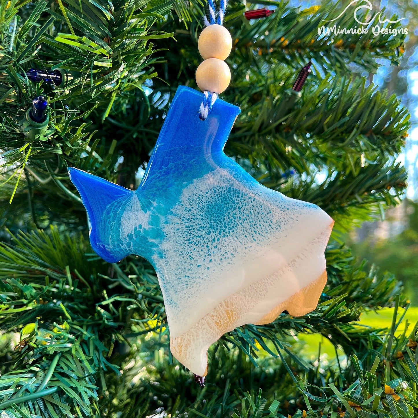 Texas-shaped wooden Christmas ornament covered in blue and teal colored ocean resin art resembling the waves along Texas' Gulf Coast. Finished with blue and white baker's twine and two wooden beads.