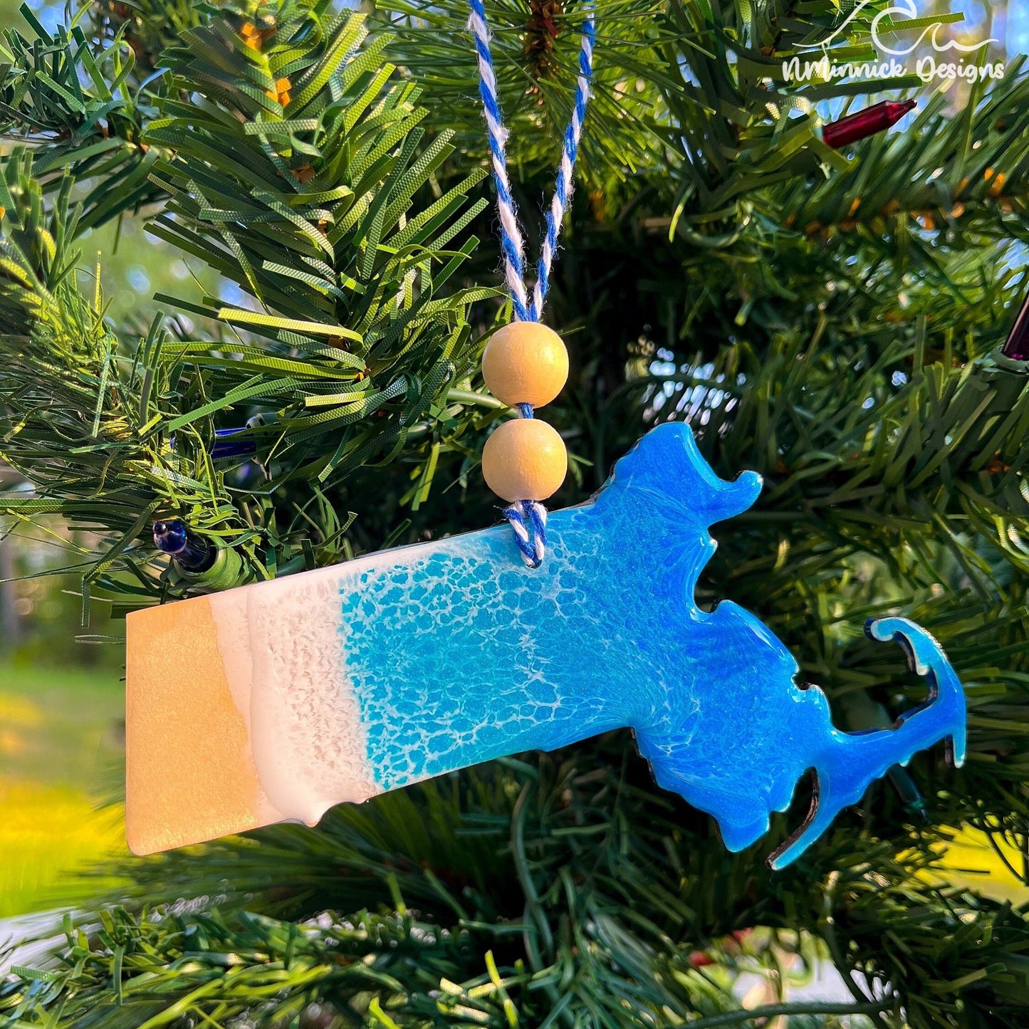 Massachusetts-shaped wooden Christmas ornament covered in blue and teal colored ocean resin art resembling the waves along Massachusetts' Atlantic Coast. Finished with blue and white baker's twine and two wooden beads.