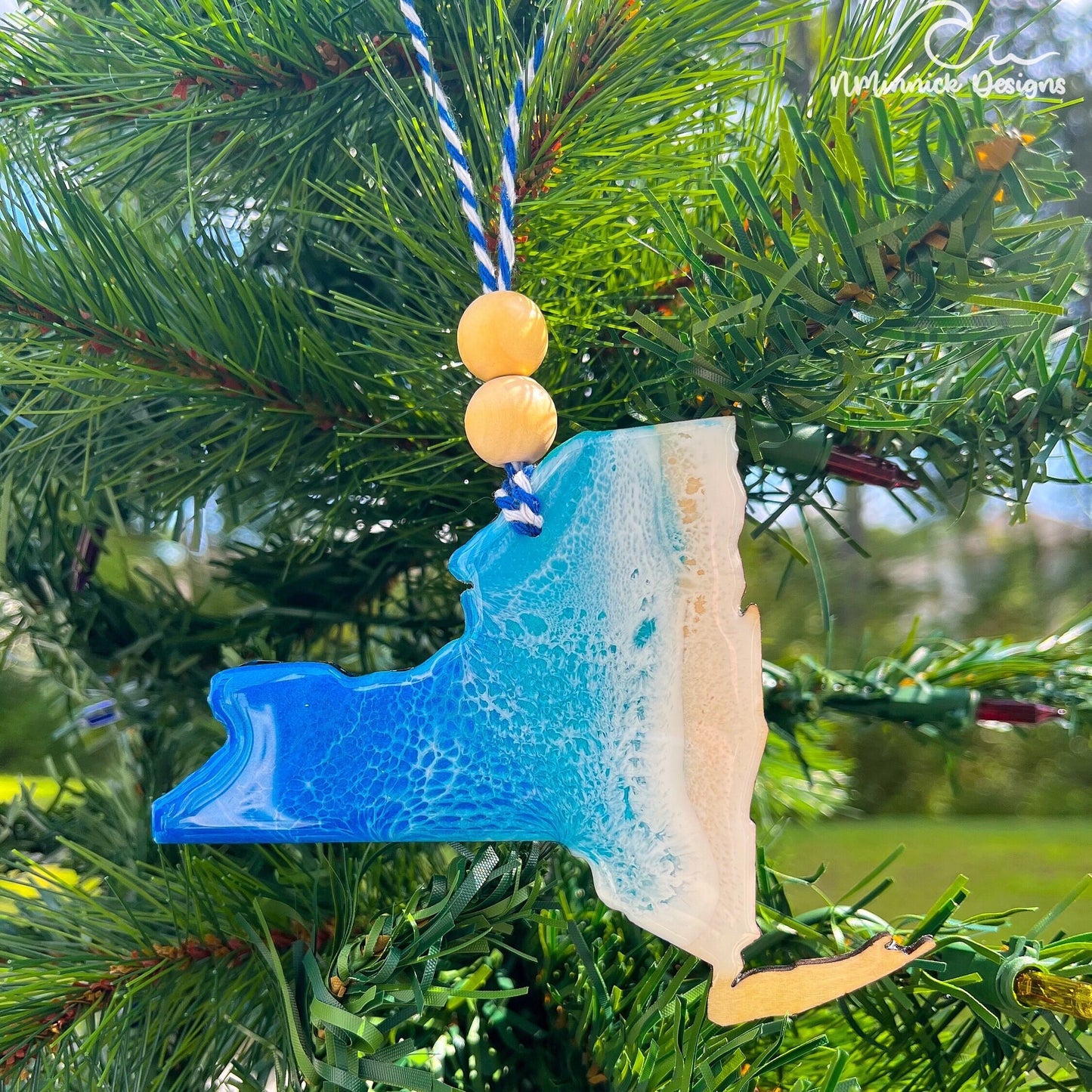a new-york state shaped wooden christmas ornament covered in ocean blue and okinawa blue ocean resin art resembling ocean waves. Finished with baker's twine and two wooden beads and hanging on a tree.