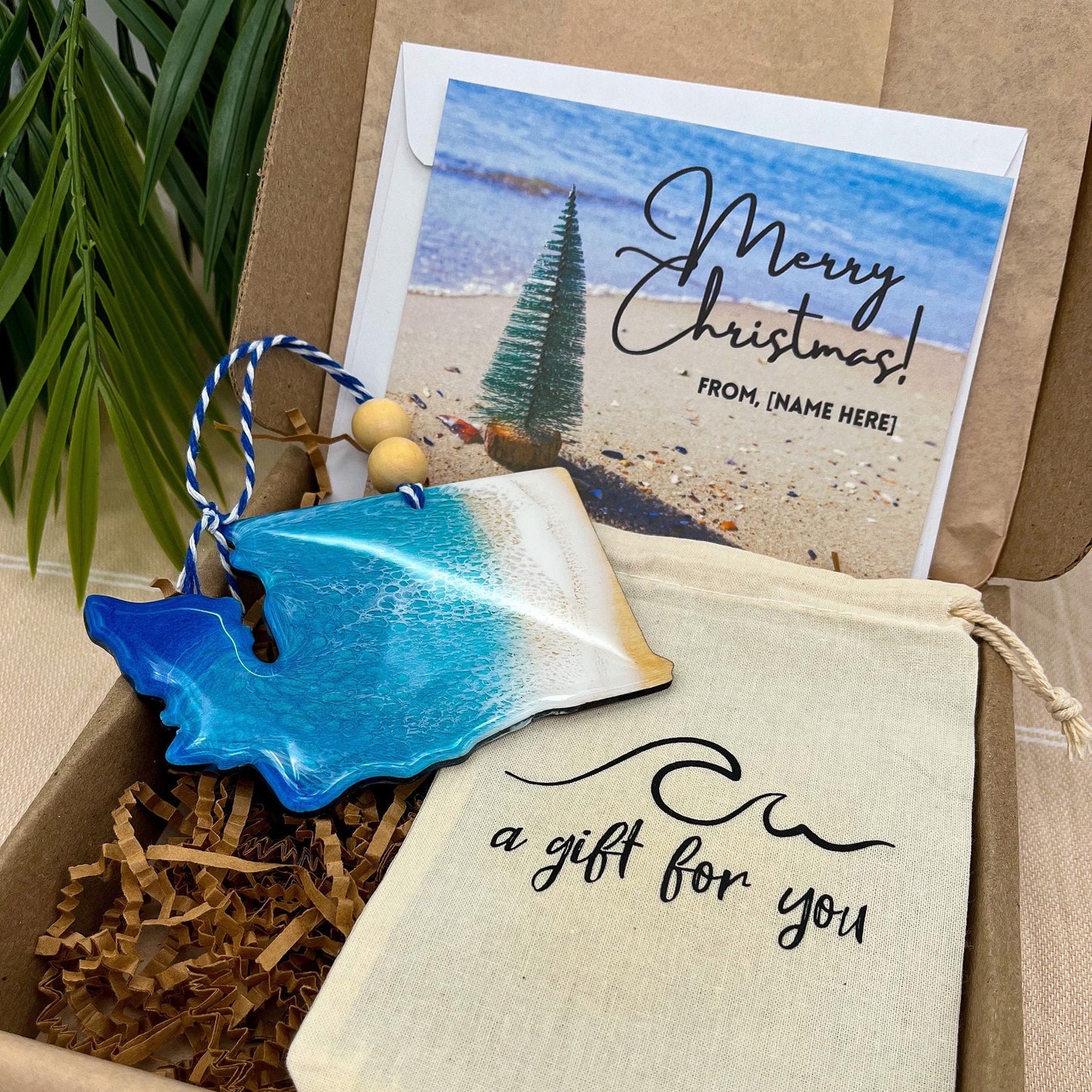A Washington state shaped wooden christmas ornament with ocean resin art, resembling the waves of the ocean. In a box with an ornament keepsake bag with a wave that says "a gift for you" and a Merry Christmas custom card.