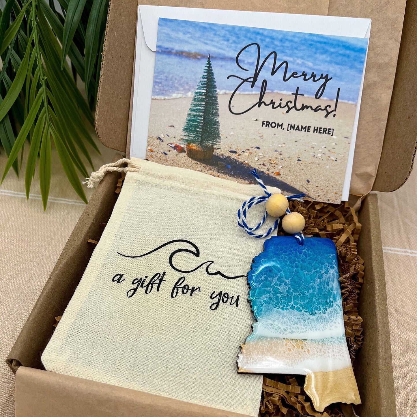A Mississippi shaped wooden christmas ornament with ocean resin art, resembling the waves of the ocean. In a box with an ornament keepsake bag with a wave that says "a gift for you" and a Merry Christmas custom card.
