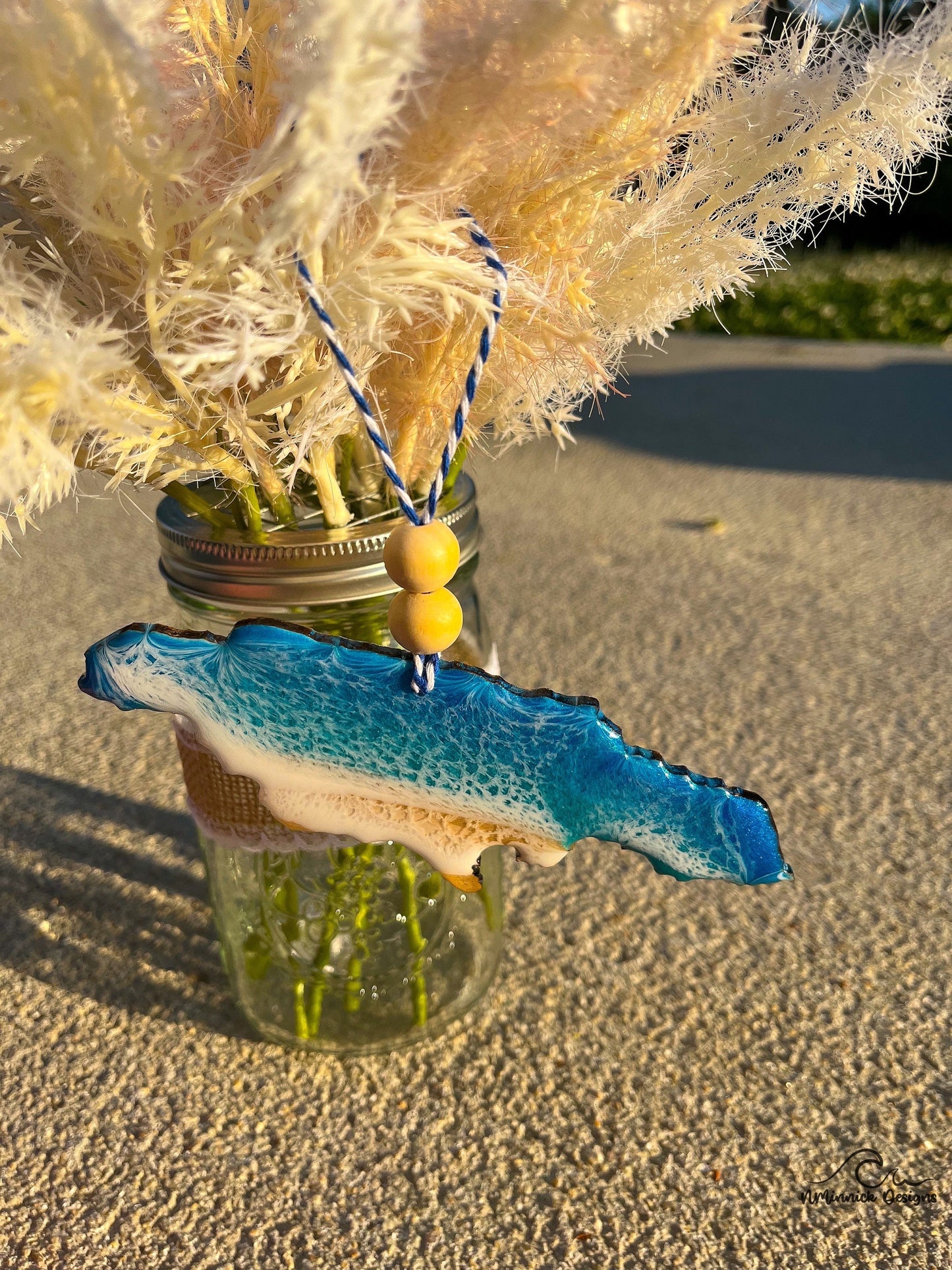 Jamaica Ocean Resin Ornament hanging against palm leaves and a mason jar