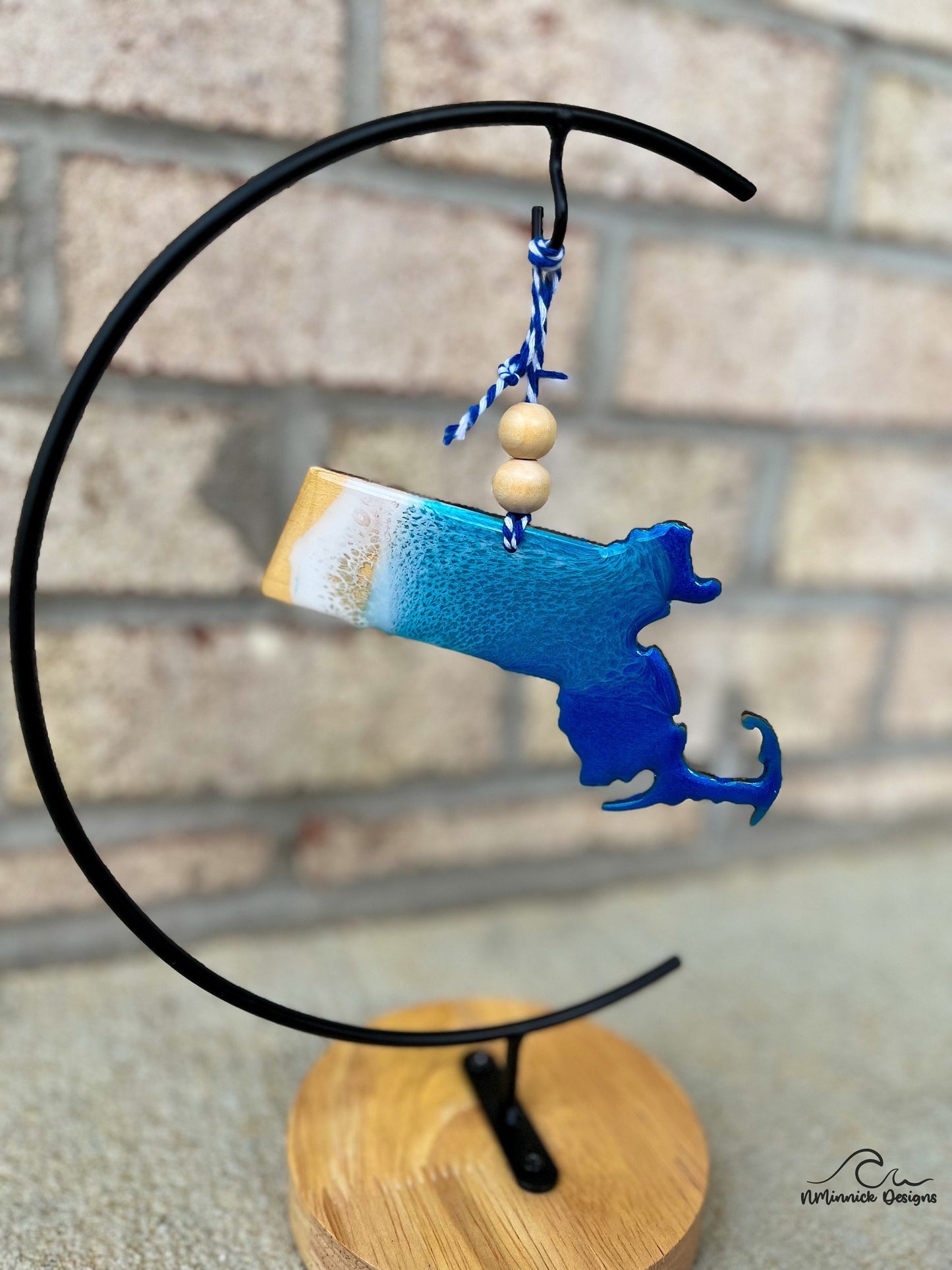 Massachusetts shaped wooden ornament with ocean resin art and hanging from an ornament stand.