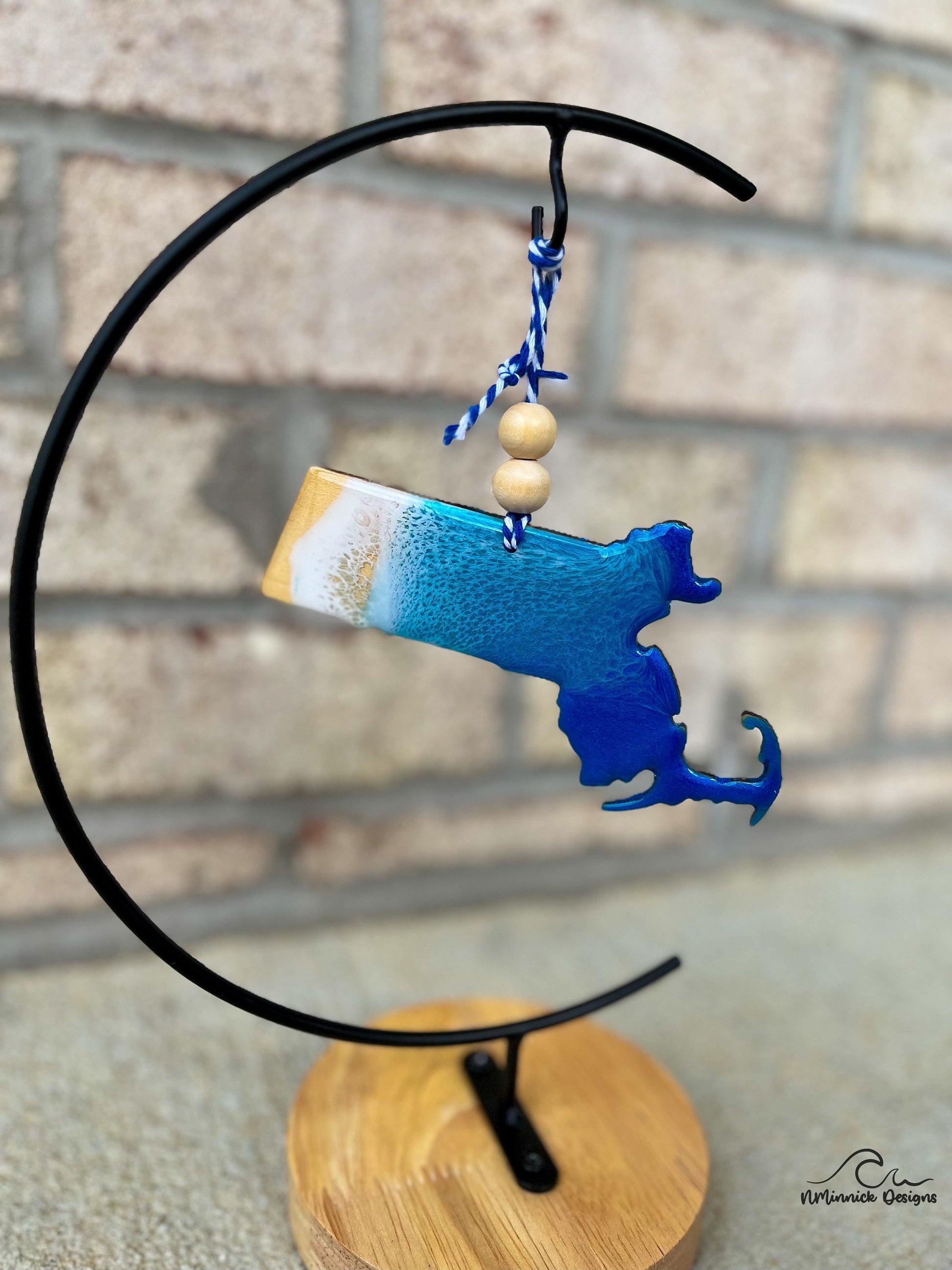 Massachusetts shaped wooden ornament with ocean resin art and hanging from an ornament stand.