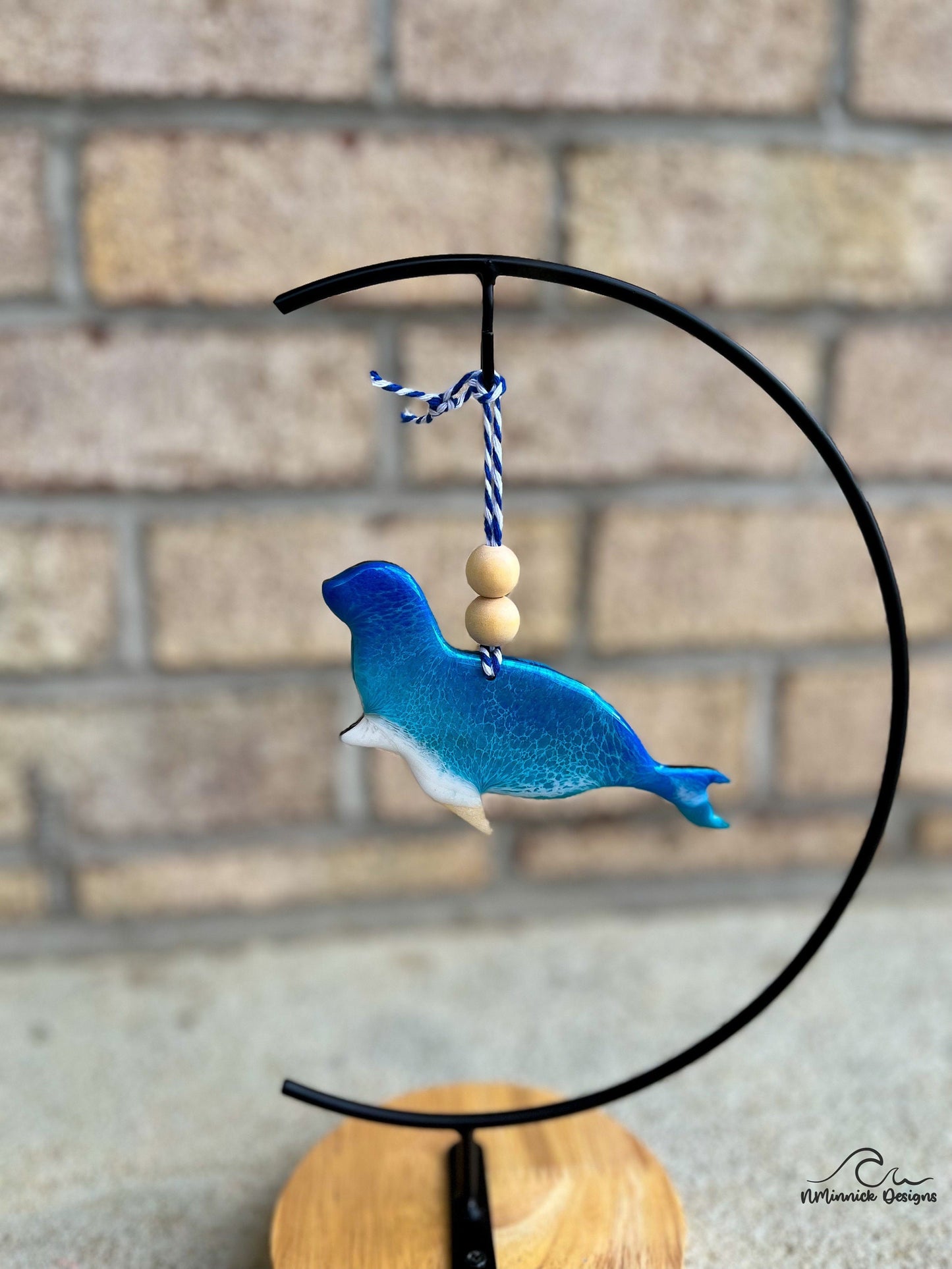 Seal shaped ornament made with wood and resin made to look like ocean waves. Hanging from an ornament stand.