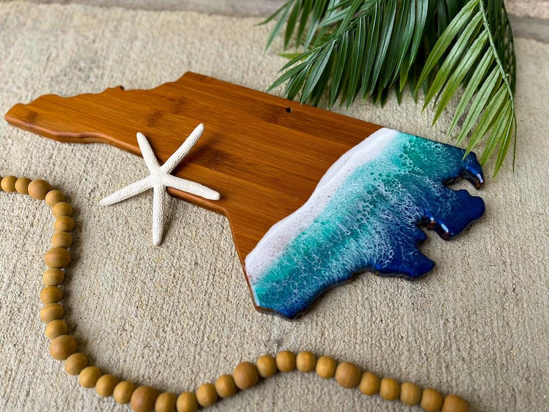 North Carolina shaped bamboo charcuterie board with dark blue and teal ocean resin art on the coastal edge of the board.