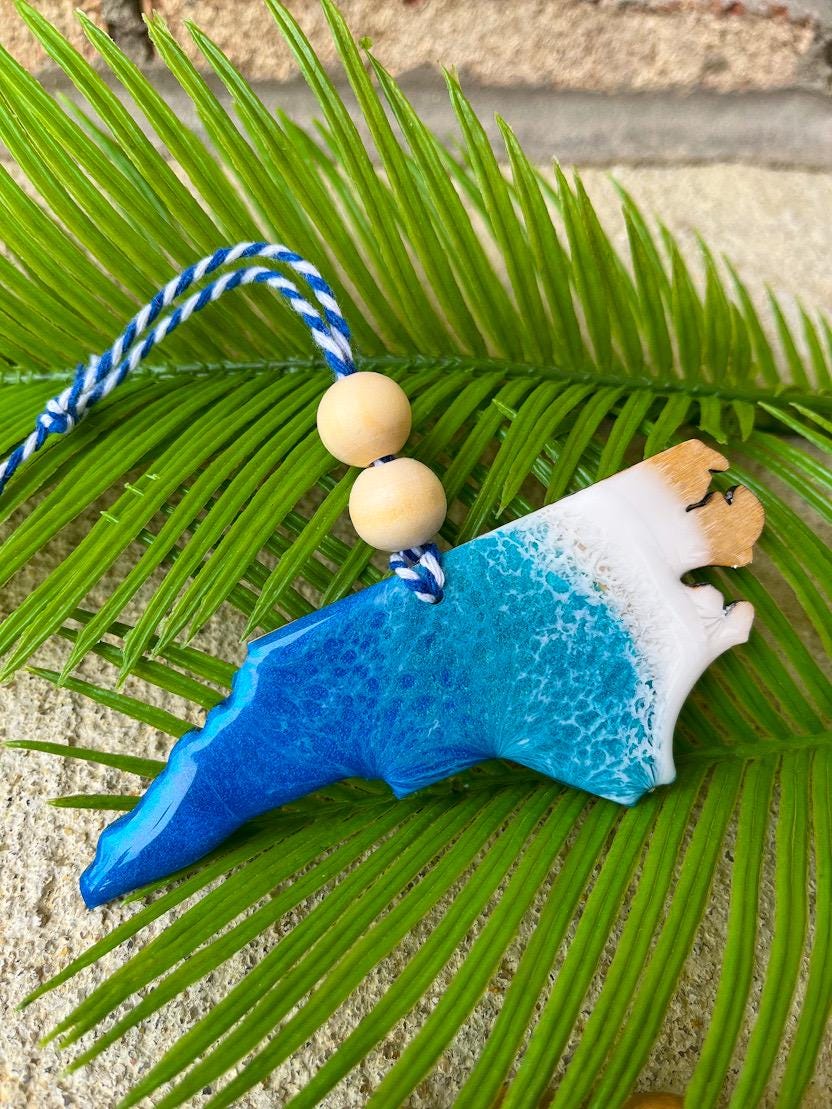 North Carolina shaped wooden ornament with an epoxy resin blue ocean wave design. Finished with two wooden beads and blue and white twine.