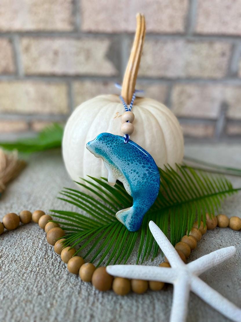 Handmade ocean resin manatee ornament resting on a white pumpkin, coastal fall decor with beach-inspired colors