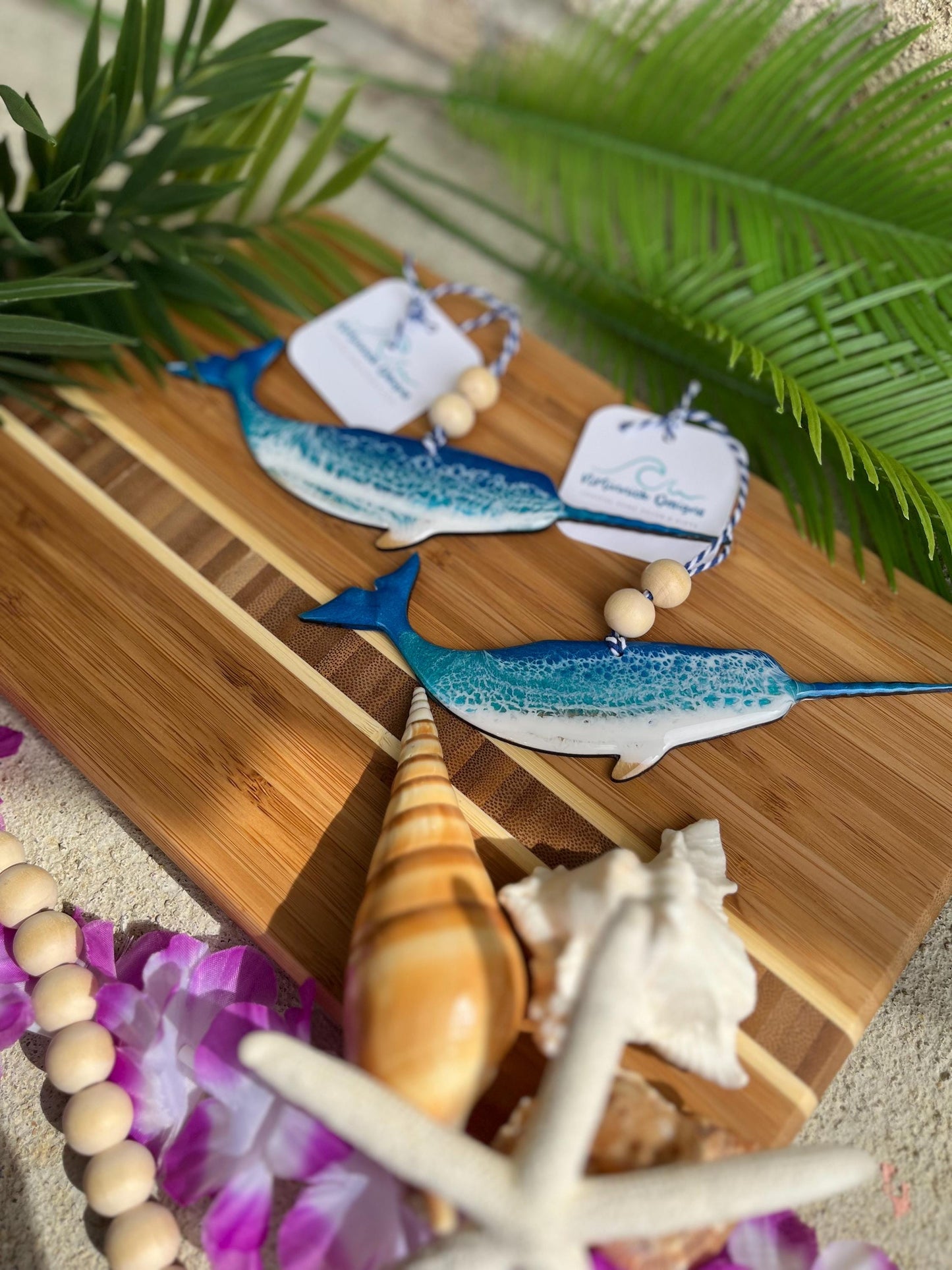Narwhal Ornaments laying against a bamboo board and palm leaves