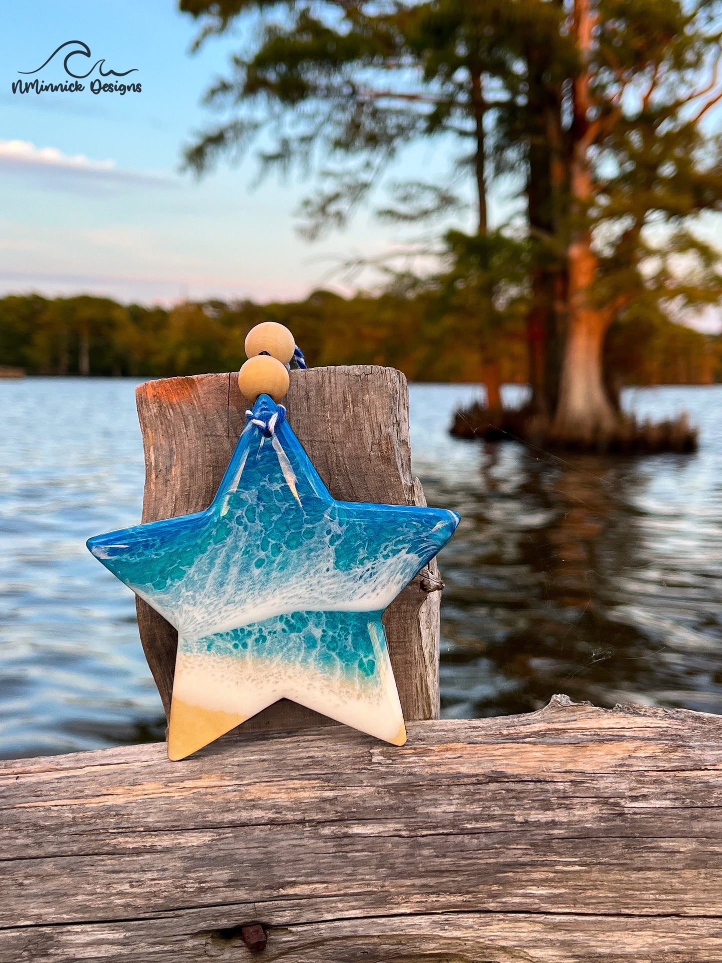 Star-shaped wooden Christmas ornament covered in blue and teal ocean resin art resembling the waves of the ocean. Finished with blue and white baker's twine and two wooden beads