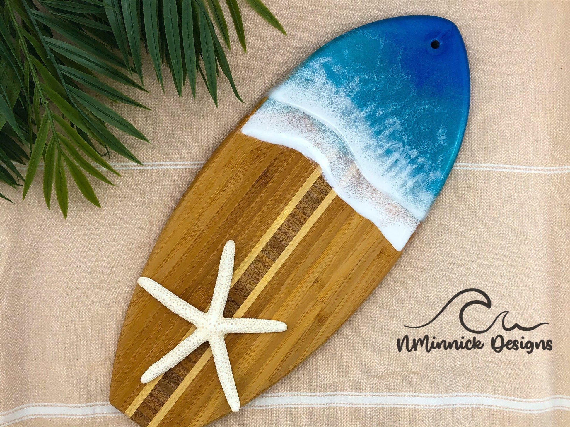14.5 inch x 6 inch bamboo surfboard shaped charcuterie serving board with a dark ocean blue and okinawa blue epoxy resin ocean scene on the top third of the board.