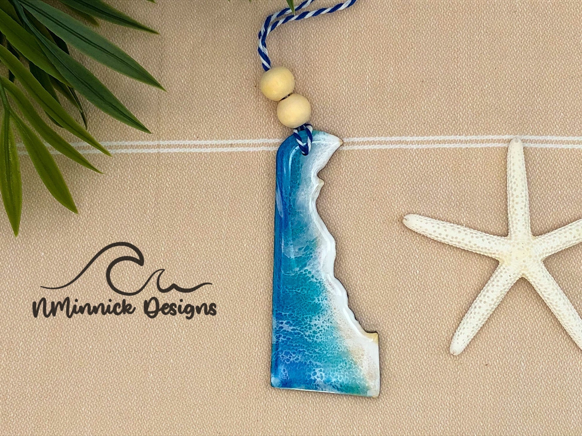 Delaware shaped wood ornament covered in blue, teal, and white resin to create a one of a kind beach scene.  Approx. 4 inches long and finished with bakers twine and two wooden beads.