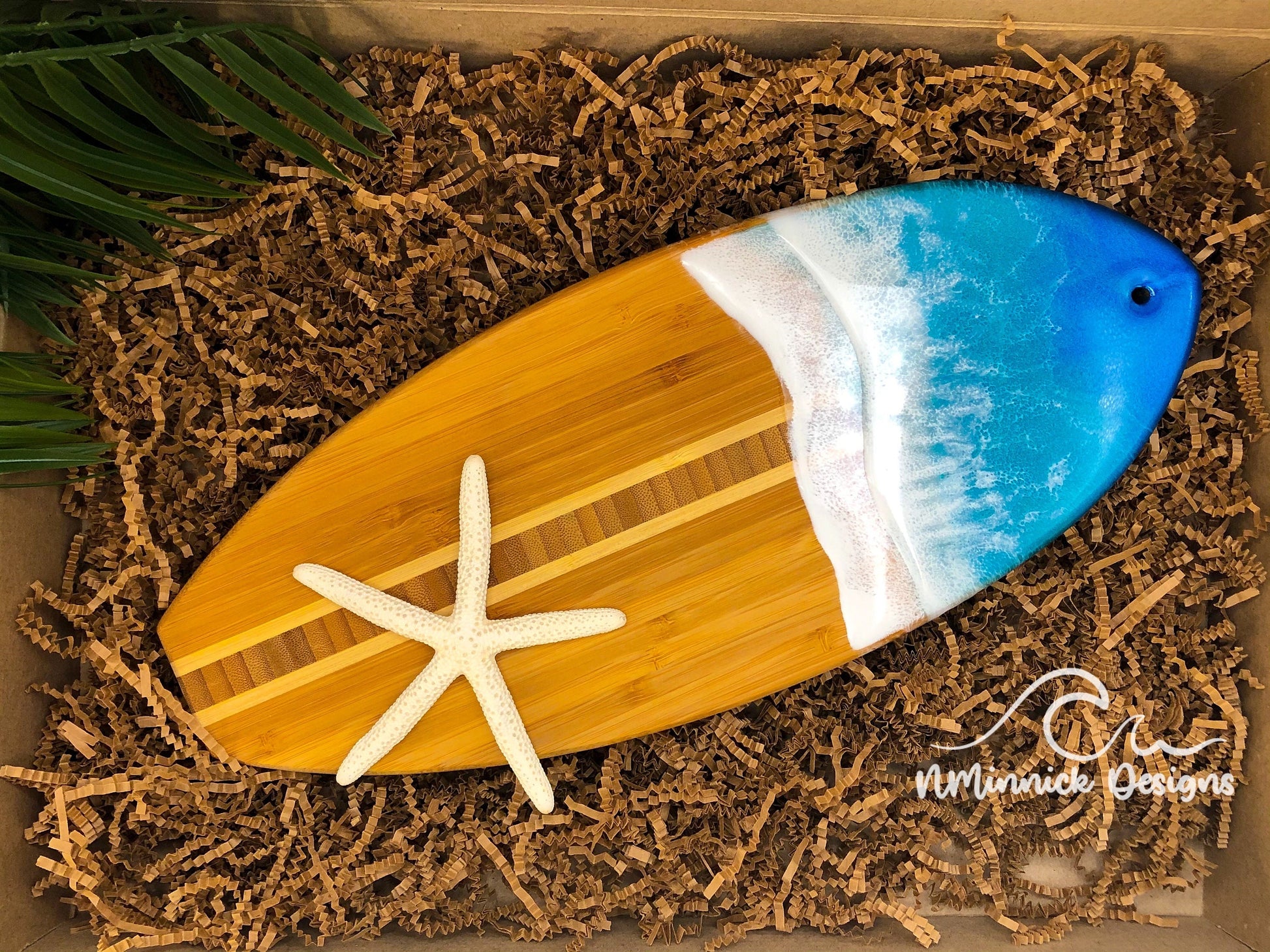 an ocean resin surfboard serving tray with blue and teal ocean waves packaged in ecofriendly plastic free materials with recyclable box, tissue paper and paper shred.