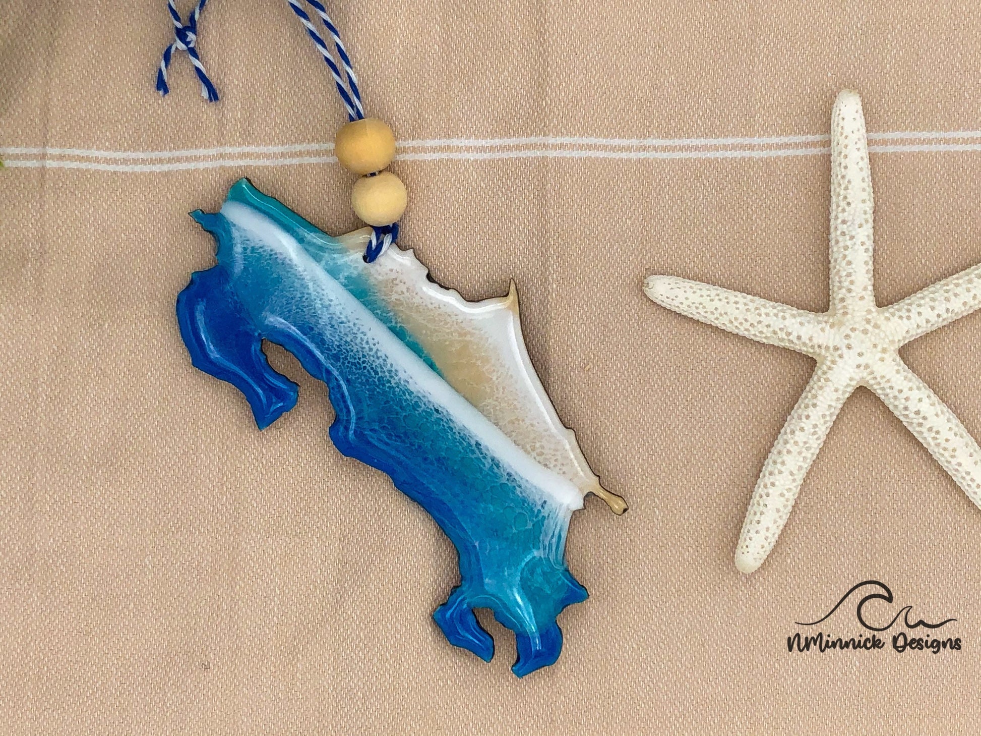 Costa Rica-shaped ornament covered in blue and teal ocean resin art resembling the waves of the ocean. Finished with blue and white baker's twice and two wooden beads.