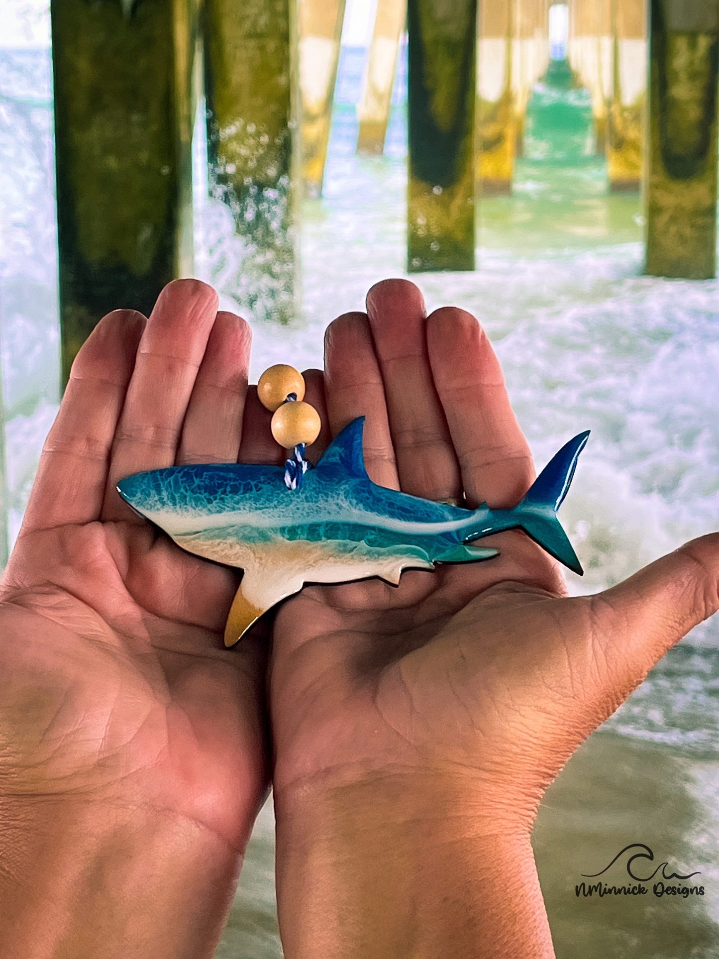 Shark-shaped wooden Christmas ornament covered in blue and teal ocean resin art resembling the waves of the ocean. Finished with blue and white baker&#39;s twine and two wooden beads.