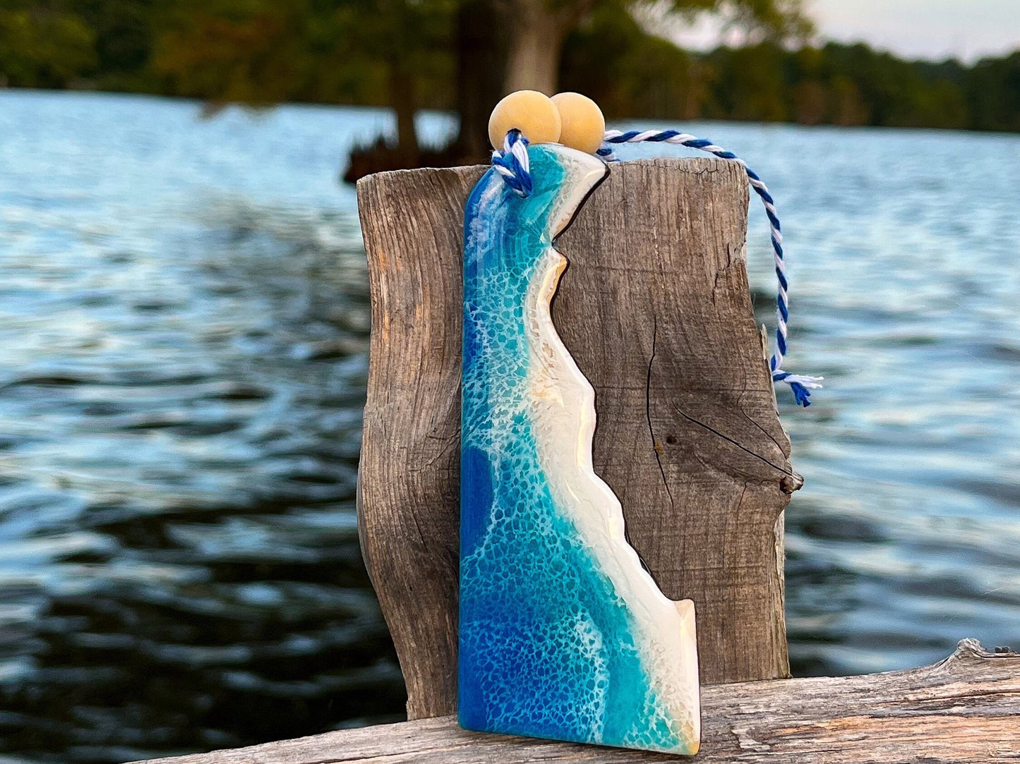 Delaware-shaped wooden Christmas ornament covered in blue and teal colored ocean resin art resembling the waves along Delaware's Atlantic Coast. Finished with blue and white baker's twine and two wooden beads.