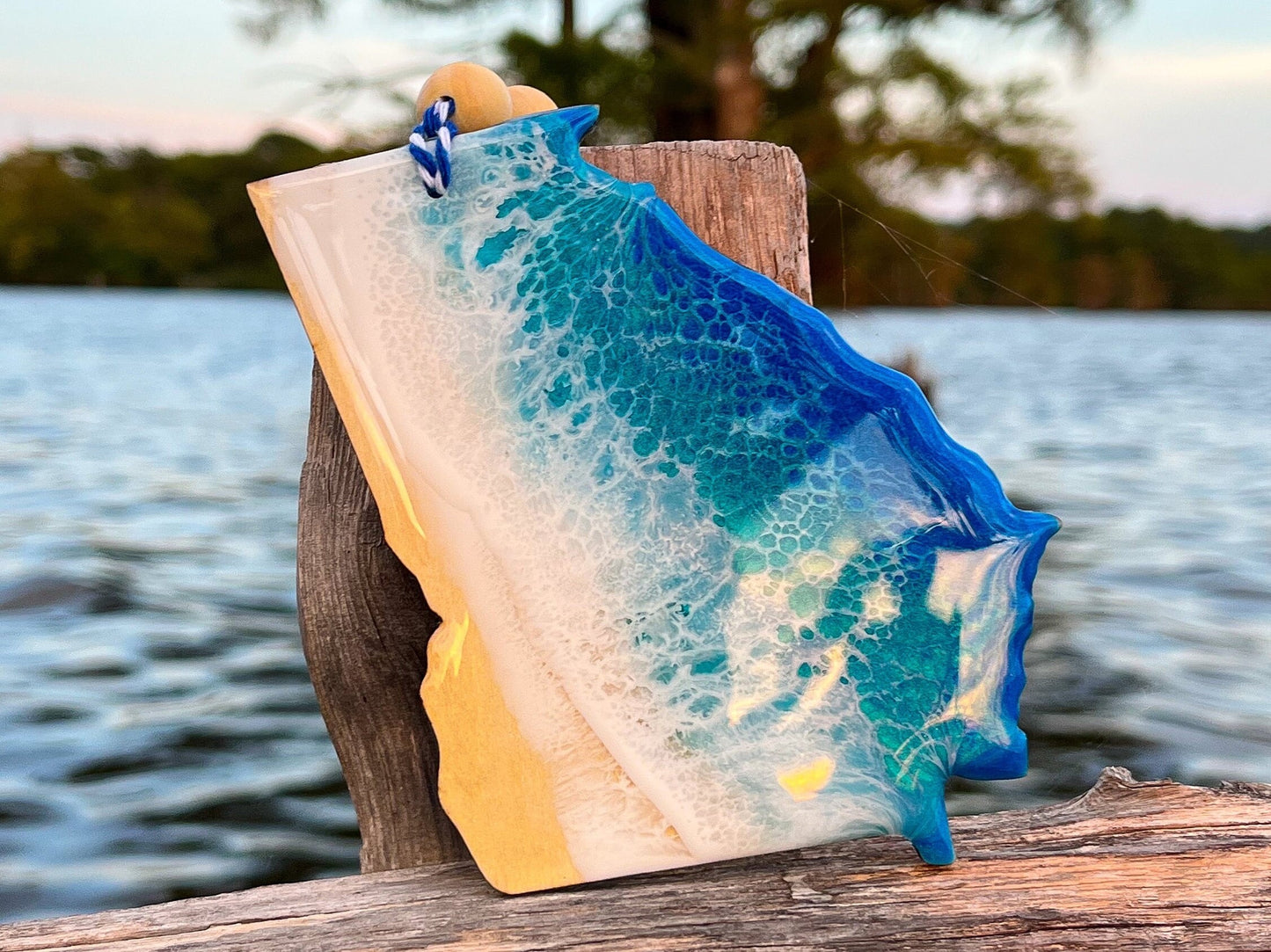 Georgia-shaped wooden Christmas ornament covered in blue and teal colored ocean resin art resembling the waves along Georgia's Coast. Finished with blue and white baker's twine and two wooden beads.