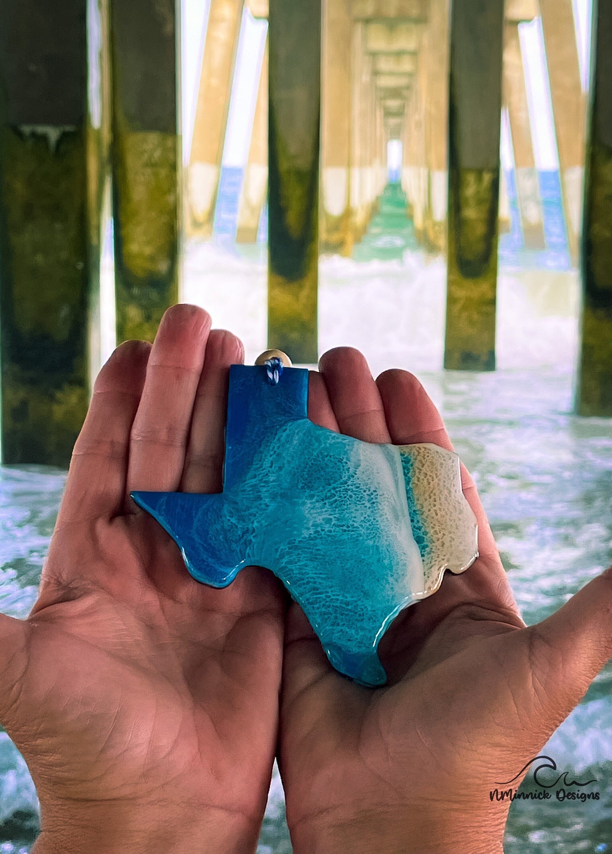 Texas-shaped wooden Christmas ornament covered in blue and teal colored ocean resin art resembling the waves along Texas' Gulf Coast. Finished with blue and white baker's twine and two wooden beads.