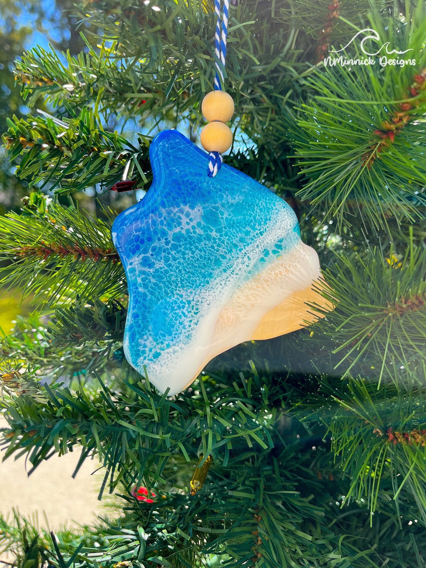 Handmade Hawaii ocean resin ornament resting on a Christmas tree, tropical beach-inspired design with ocean wave details