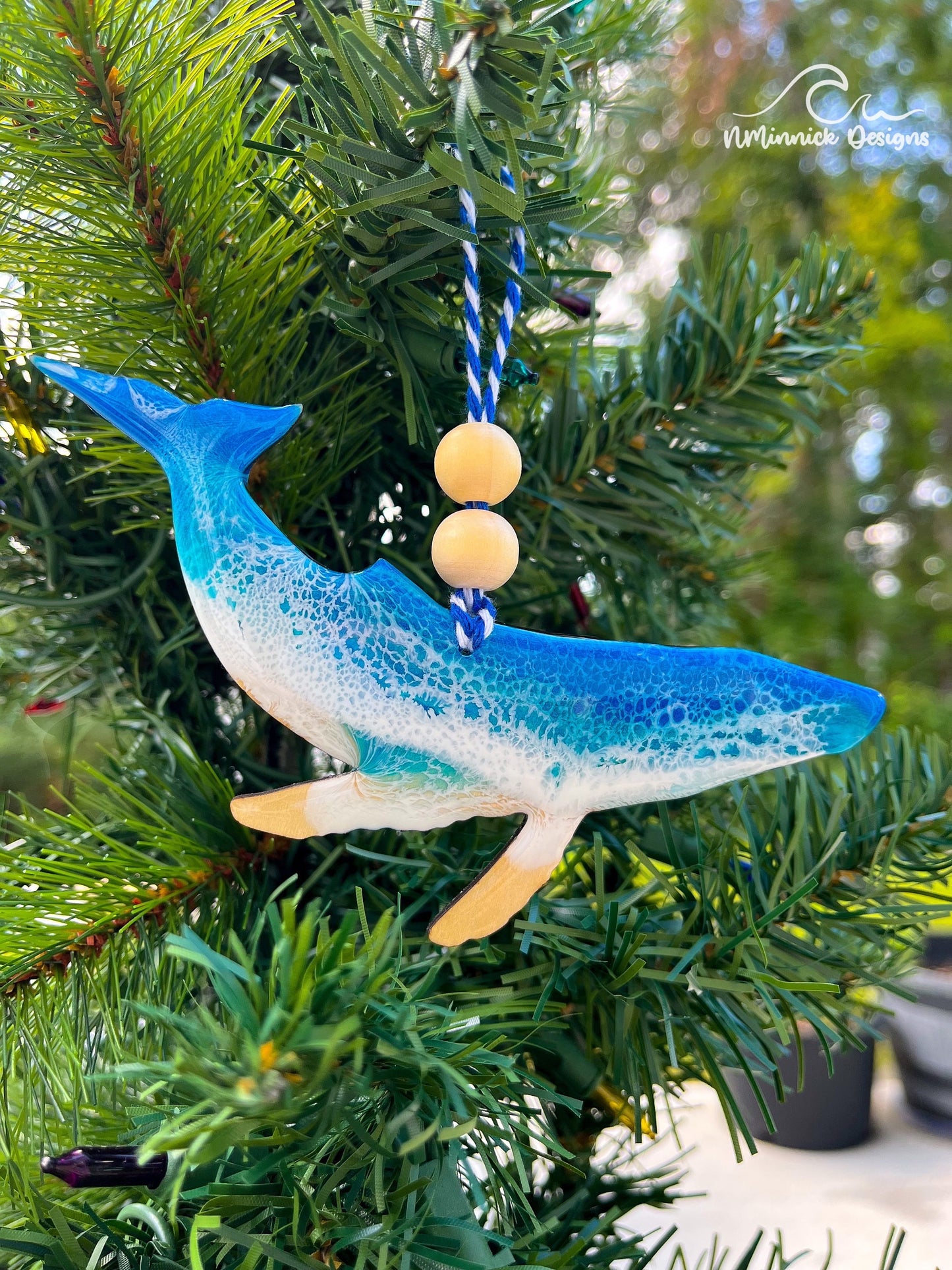 Handmade humpback whale ocean resin ornament resting on a Christmas tree, coastal beach-inspired design with ocean wave details