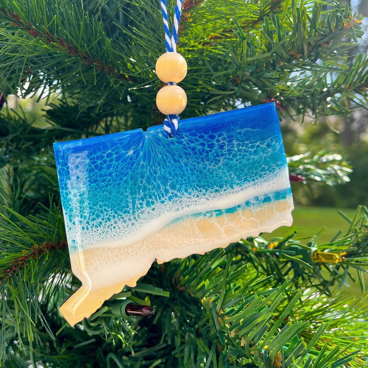 Connecticut Ornament with blue and white ocean resin art hanging on a tree.
