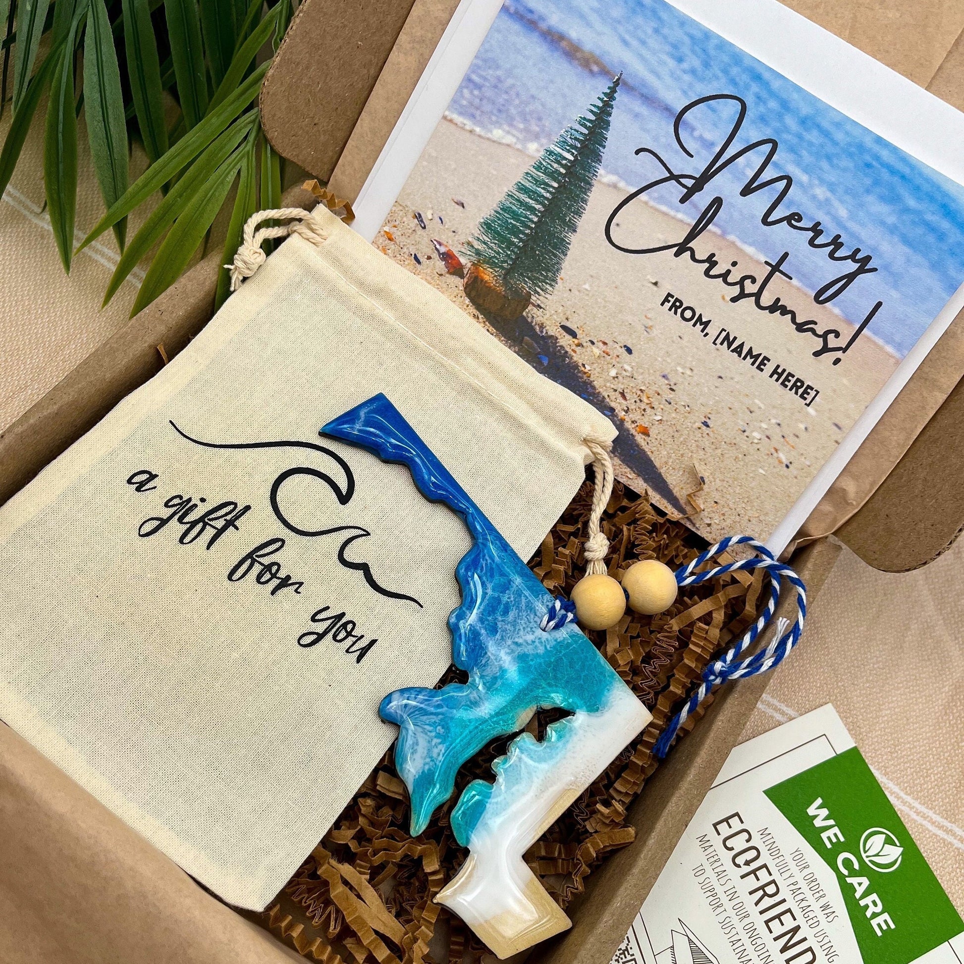 A Maryland shaped wooden christmas ornament with ocean resin art, resembling the waves of the ocean. In a box with an ornament keepsake bag with a wave that says &quot;a gift for you&quot; and a Merry Christmas custom card.