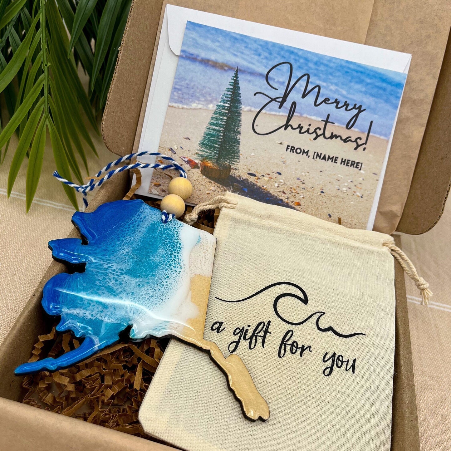 An Alaska shaped wooden christmas ornament with ocean resin art, resembling the waves of the ocean. In a box with an ornament keepsake bag with a wave that says &quot;a gift for you&quot; and a Merry Christmas custom card.