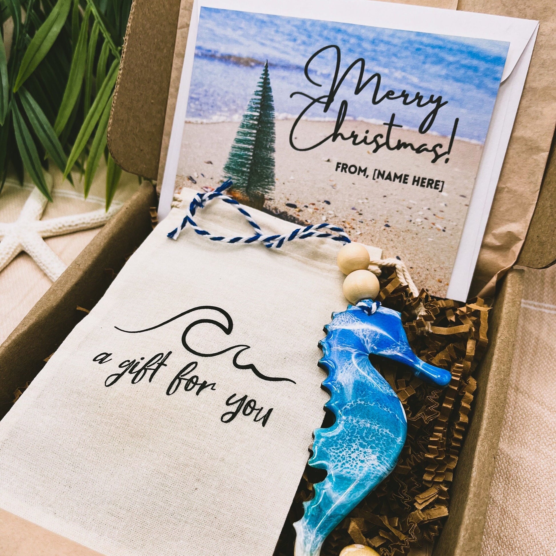 A Seahorse shaped wooden christmas ornament with ocean resin art, resembling the waves of the ocean. In a box with an ornament keepsake bag with a wave that says &quot;a gift for you&quot; and a Merry Christmas custom card.