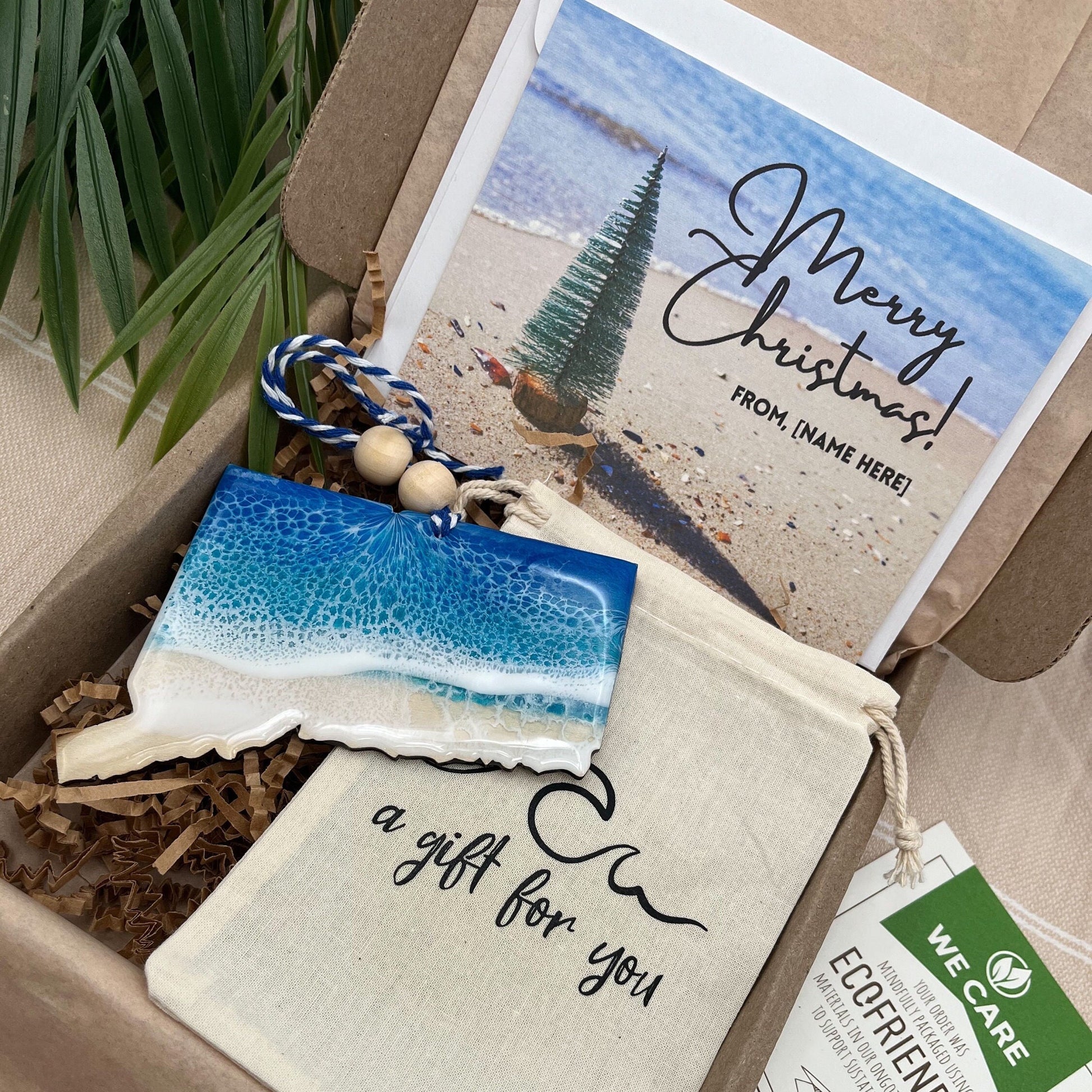 A Connecticut shaped wooden christmas ornament with ocean resin art, resembling the waves of the ocean. In a box with an ornament keepsake bag with a wave that says &quot;a gift for you&quot; and a Merry Christmas custom card.