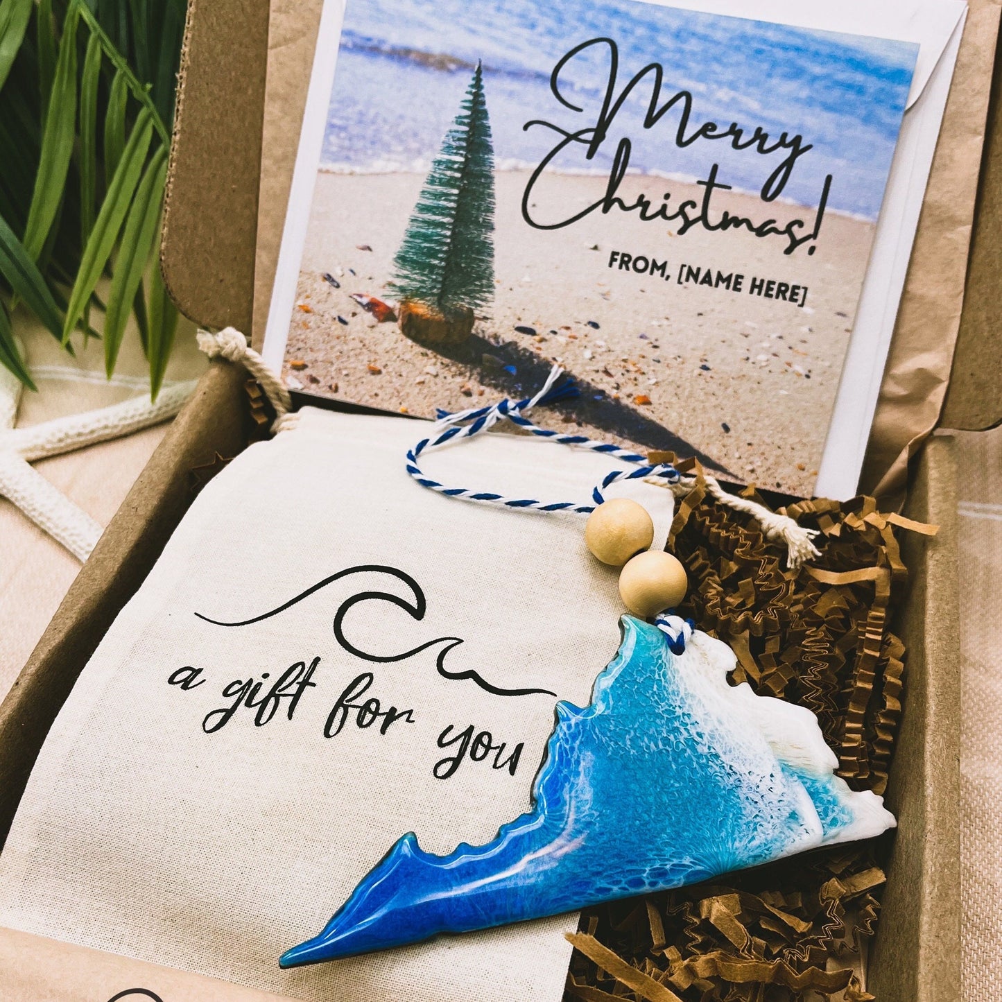 A Virginia shaped wooden christmas ornament with ocean resin art, resembling the waves of the ocean. In a box with an ornament keepsake bag with a wave that says "a gift for you" and a Merry Christmas custom card.