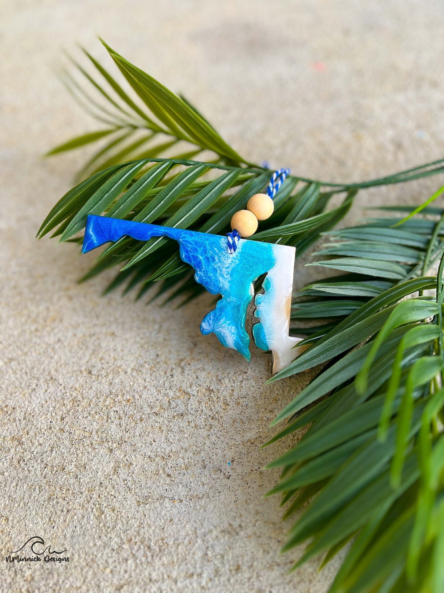 Maryland ornament with ocean resin art laying against palm leaves.