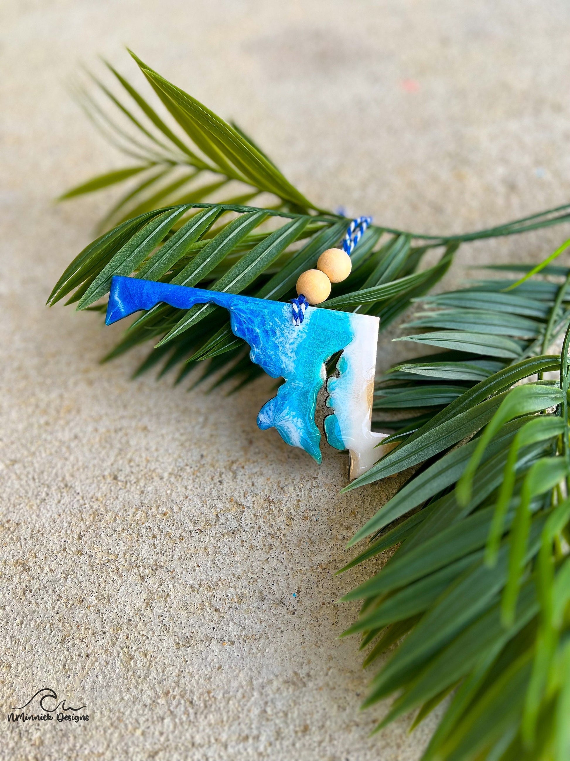 Maryland ornament with ocean resin art laying against palm leaves.