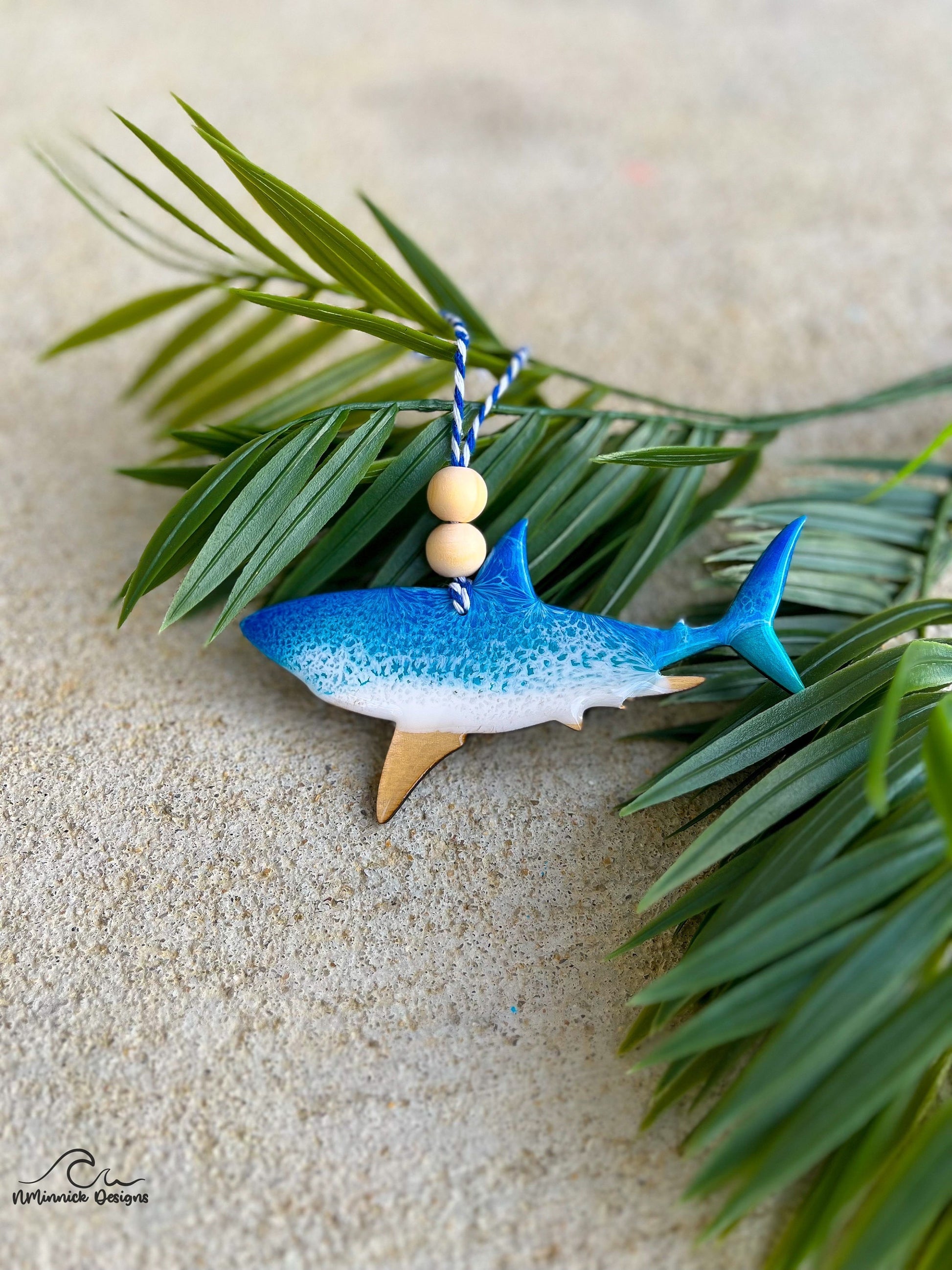 Great White Shark ornament with ocean resin art laying against palm leaves.