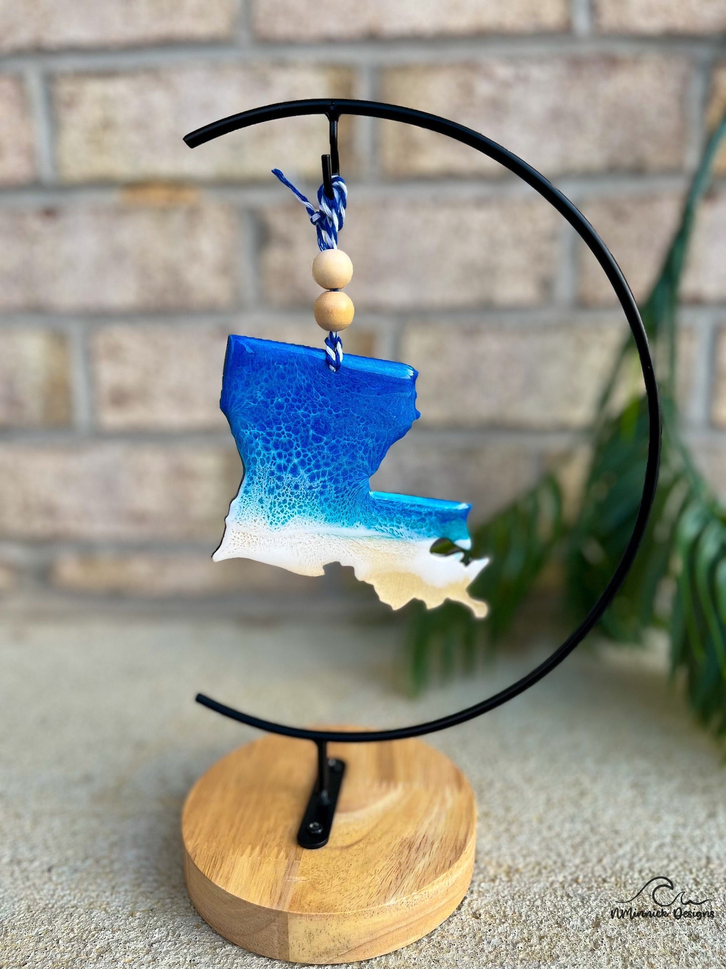 Louisiana shaped wooden ornament with ocean resin waves on the front hanging from blue and white twine with two wooden beads shown on an ornament hanger