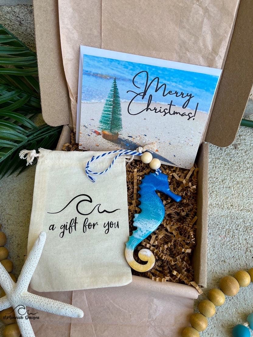 A Seahorse shaped wooden christmas ornament with ocean resin art, resembling the waves of the ocean. In a box with an ornament keepsake bag with a wave that says "a gift for you" and a Merry Christmas custom card.