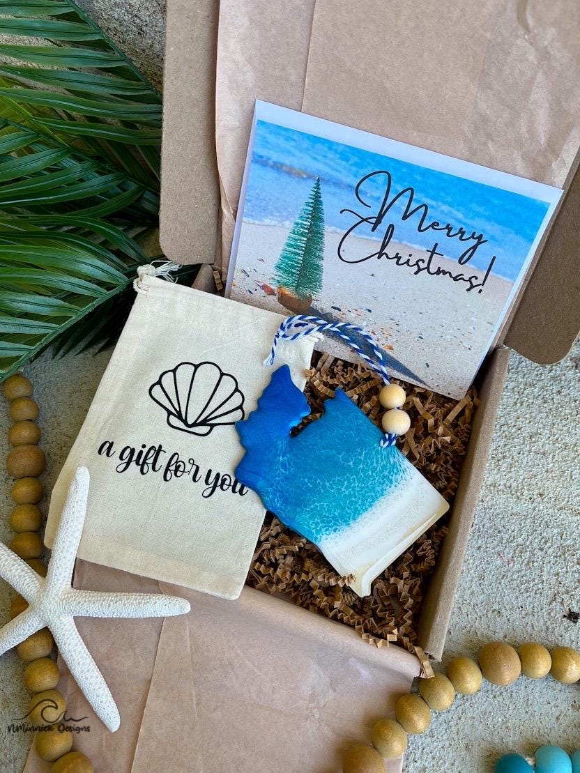 A Washington state shaped wooden christmas ornament with ocean resin art, resembling the waves of the ocean. In a box with an ornament keepsake bag with a wave that says "a gift for you" and a Merry Christmas custom card.
