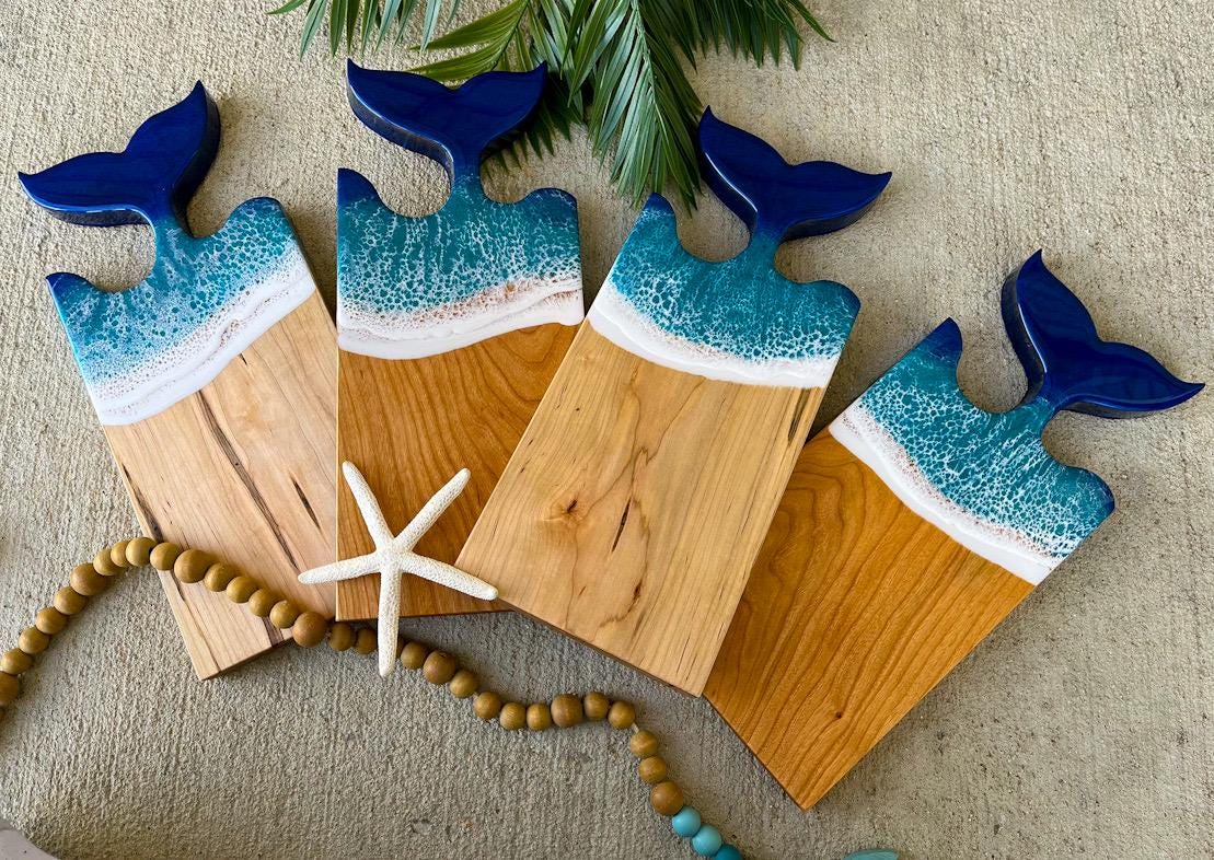 Four wooden charcuterie boards with a mermaid tail fin shape at the top and blue and teal ocean resin waves