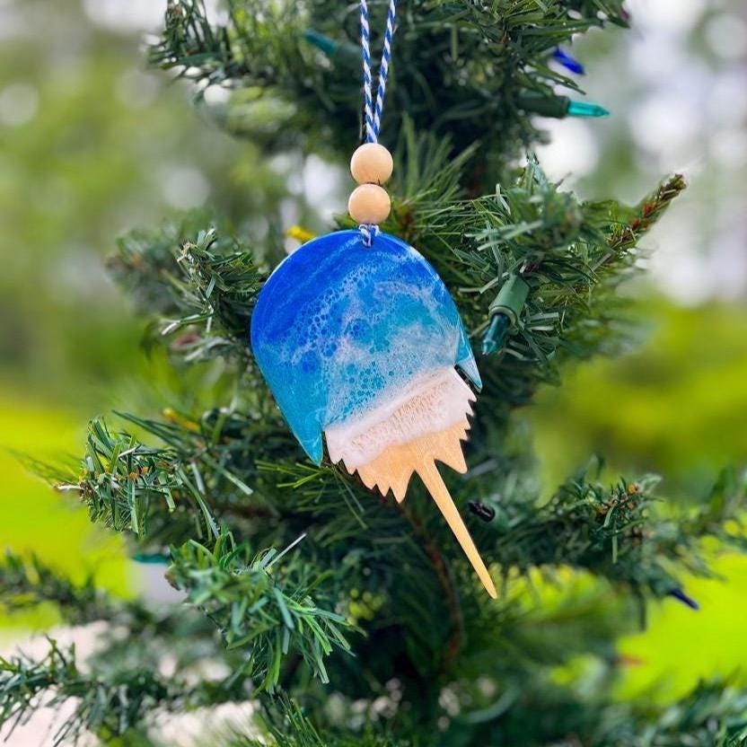 Horseshoe Crab shaped wooden ornament with blue, teal, and white ocean resin waves on top. Shown hanging on a Christmas tree.