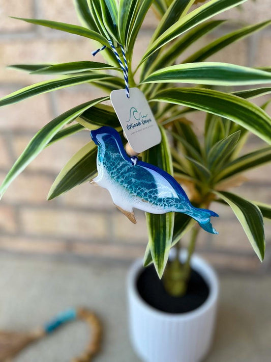 Handmade seal ocean resin ornament hanging on a tropical palm plant, coastal-inspired decor with ocean waves design