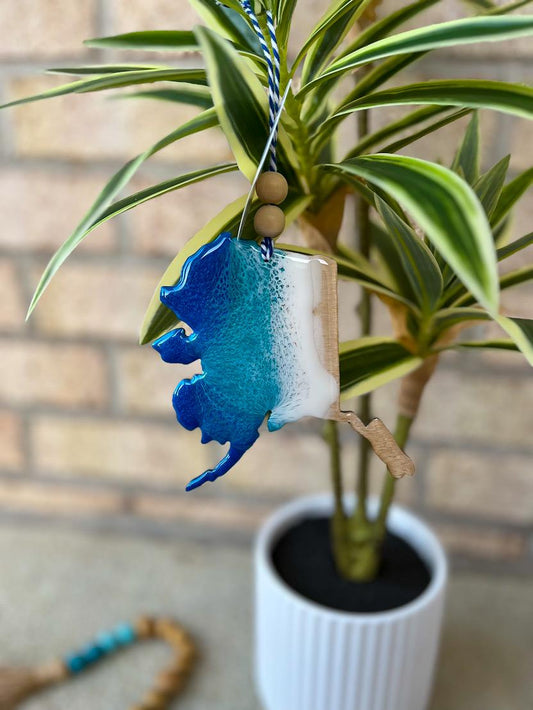 Handmade Alaska state ocean resin ornament hanging on a tropical palm plant, coastal decor with ocean-inspired wave design