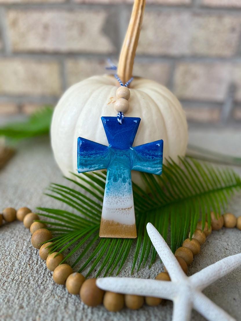 Handmade cross ocean resin ornament resting on a white pumpkin, coastal-inspired design with ocean waves