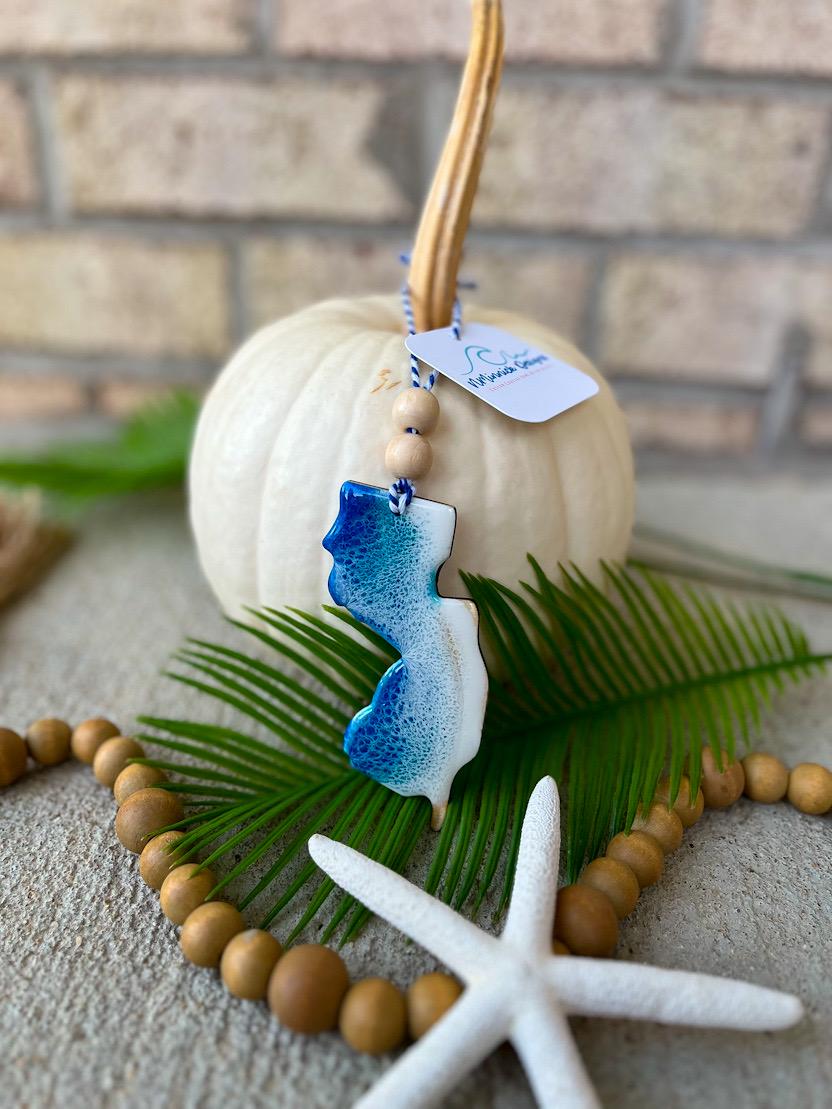 Handmade New Jersey state ocean resin ornament resting on a white pumpkin, coastal fall decor with ocean-inspired wave design