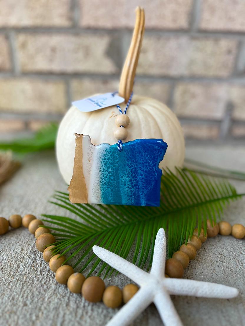 Handmade Oregon state ocean resin ornament displayed on a white pumpkin, coastal fall decor with ocean wave design