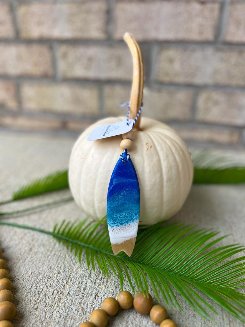 Handmade surfboard ocean resin ornament resting on a white pumpkin, coastal beach-inspired design with ocean wave details
